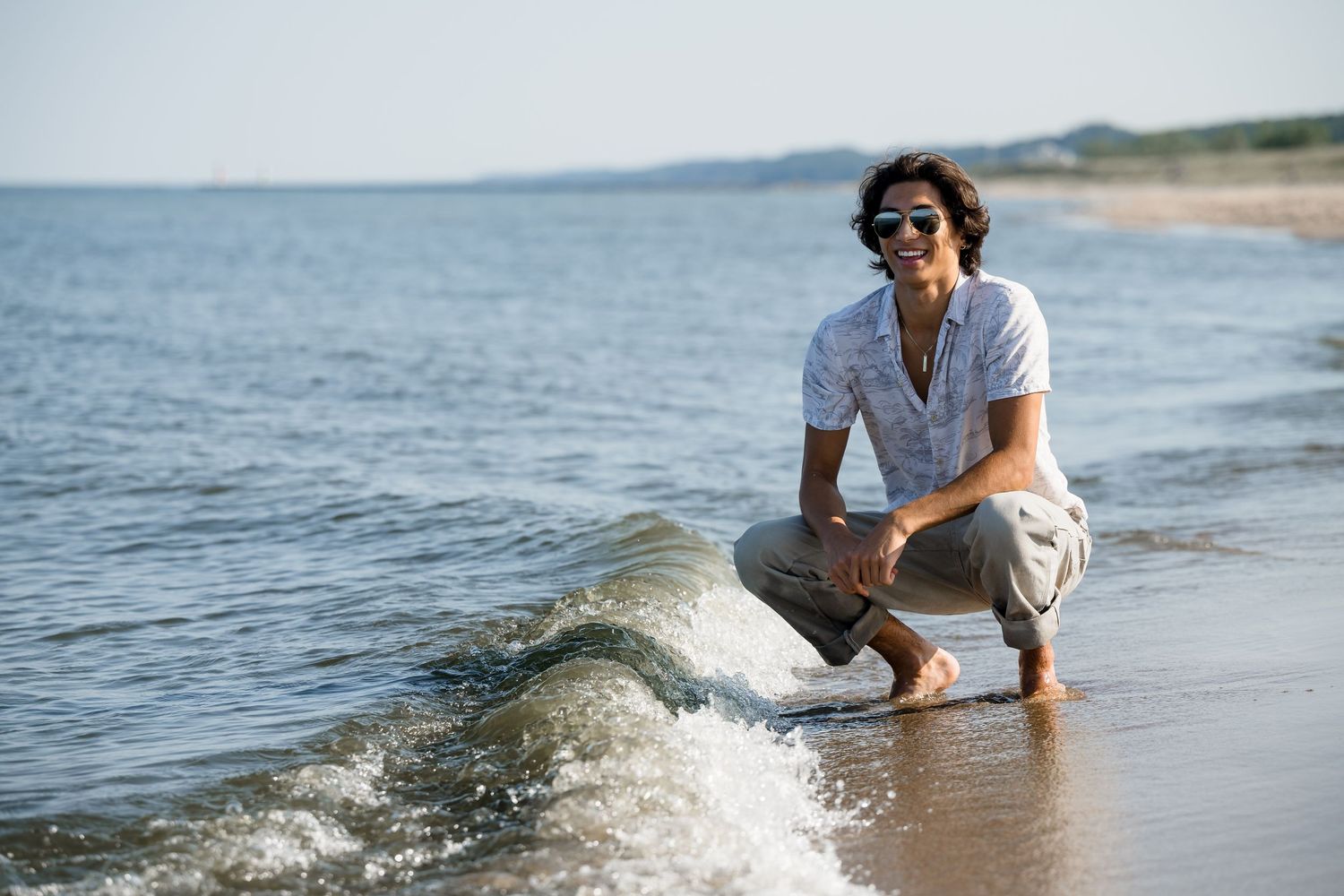 Senior boy photo session of beach at Lake Michigan with waves splashing near the shore.