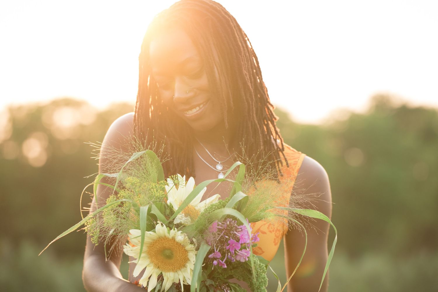 Senior girl  holds sunflowers during golden sunset in outdoor setting.