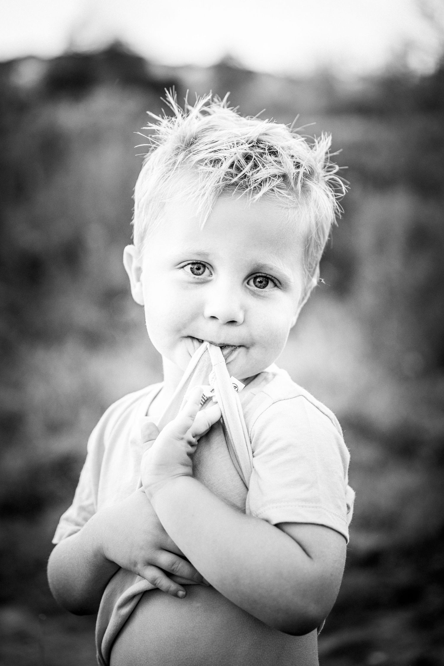 Black and white portrait of a young child with spiky hair making a playful expression with fingers near mouth.