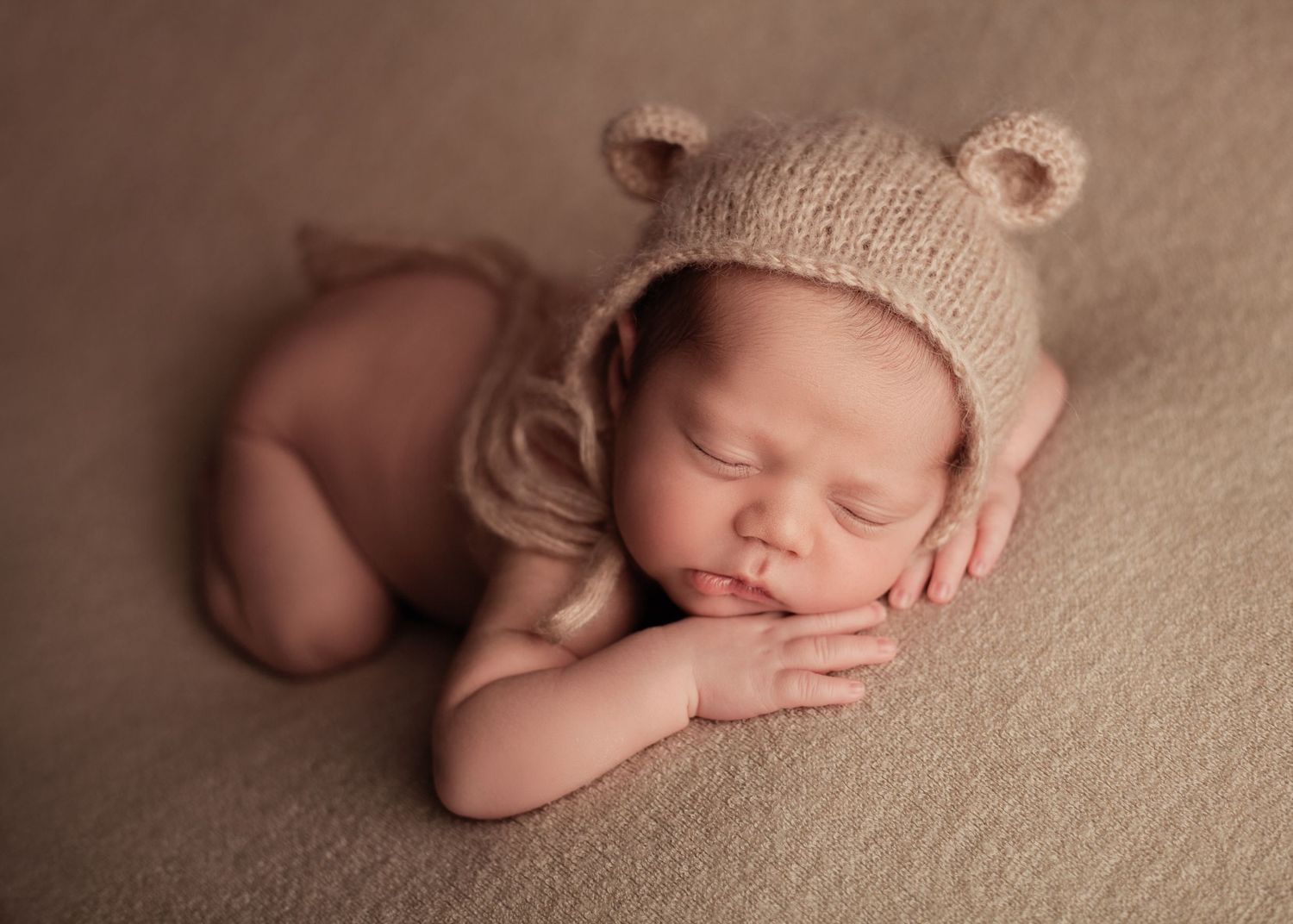 Newborn baby sleeping wrapped on a neutral beige blanket wearing a bear hat during a newborn photography session