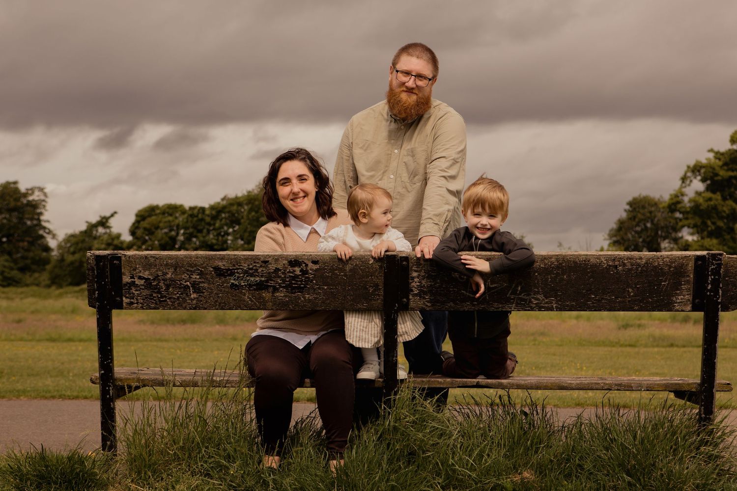 Family of four sitting together on an outdoors bench during a lifestyle photography session in Liverpool