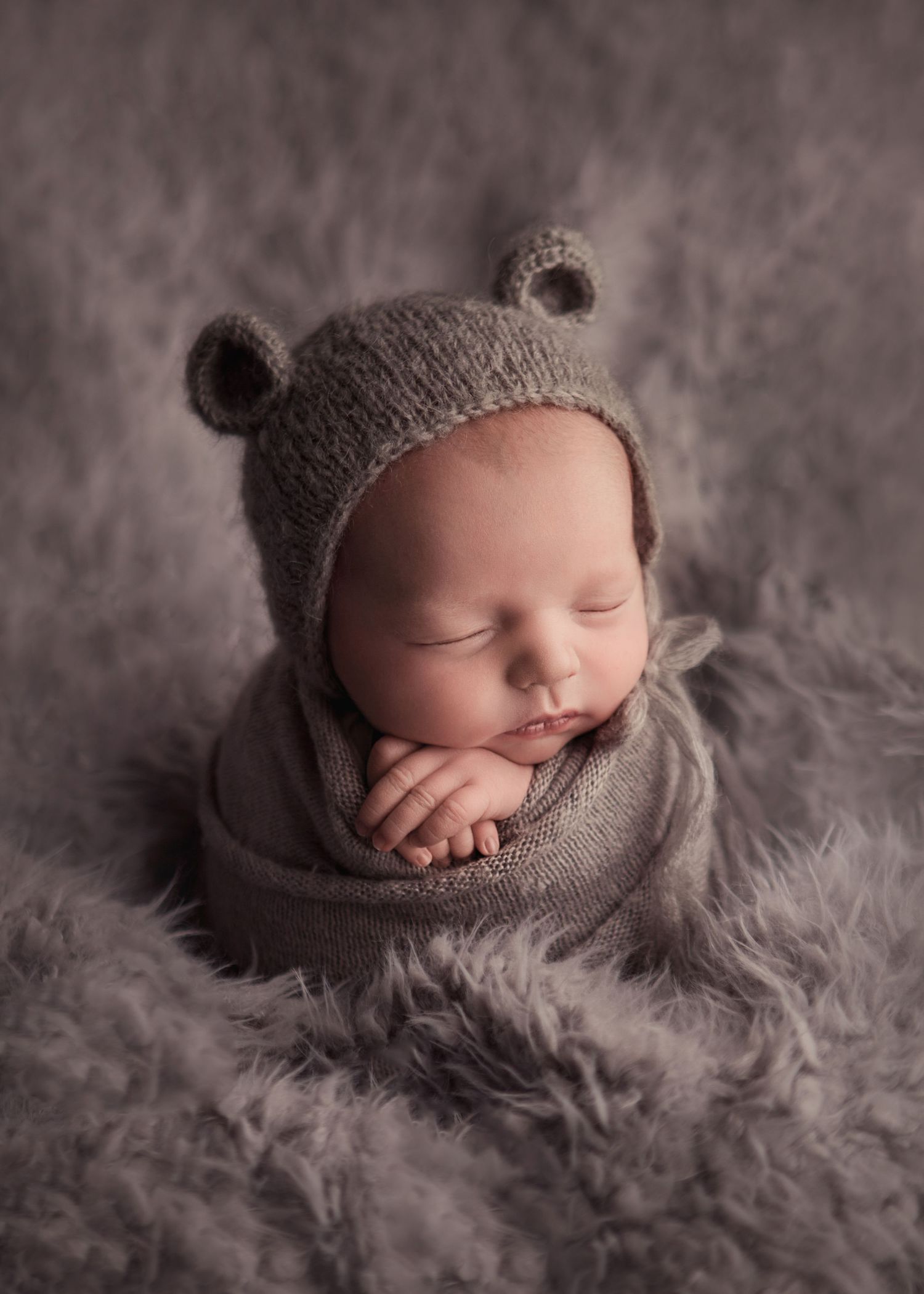 Newborn baby sleeping wrapped on a grey blanket wearing a bear hat during a newborn photography session