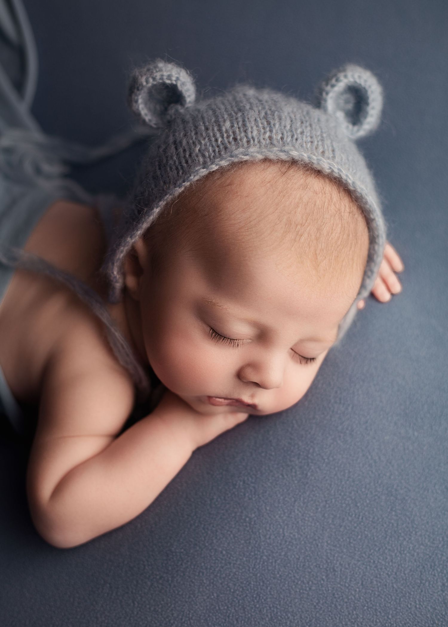 Newborn baby sleeping wrapped on a blue blanket wearing a bear hat during a newborn photography session