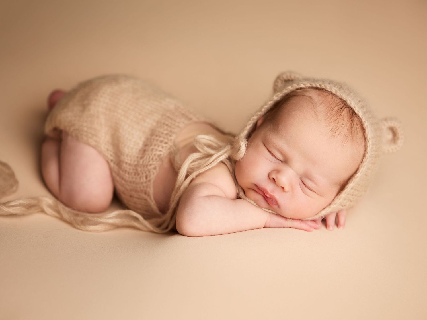 Newborn baby sleeping in a neutral romper and bear hat during a newborn photography session