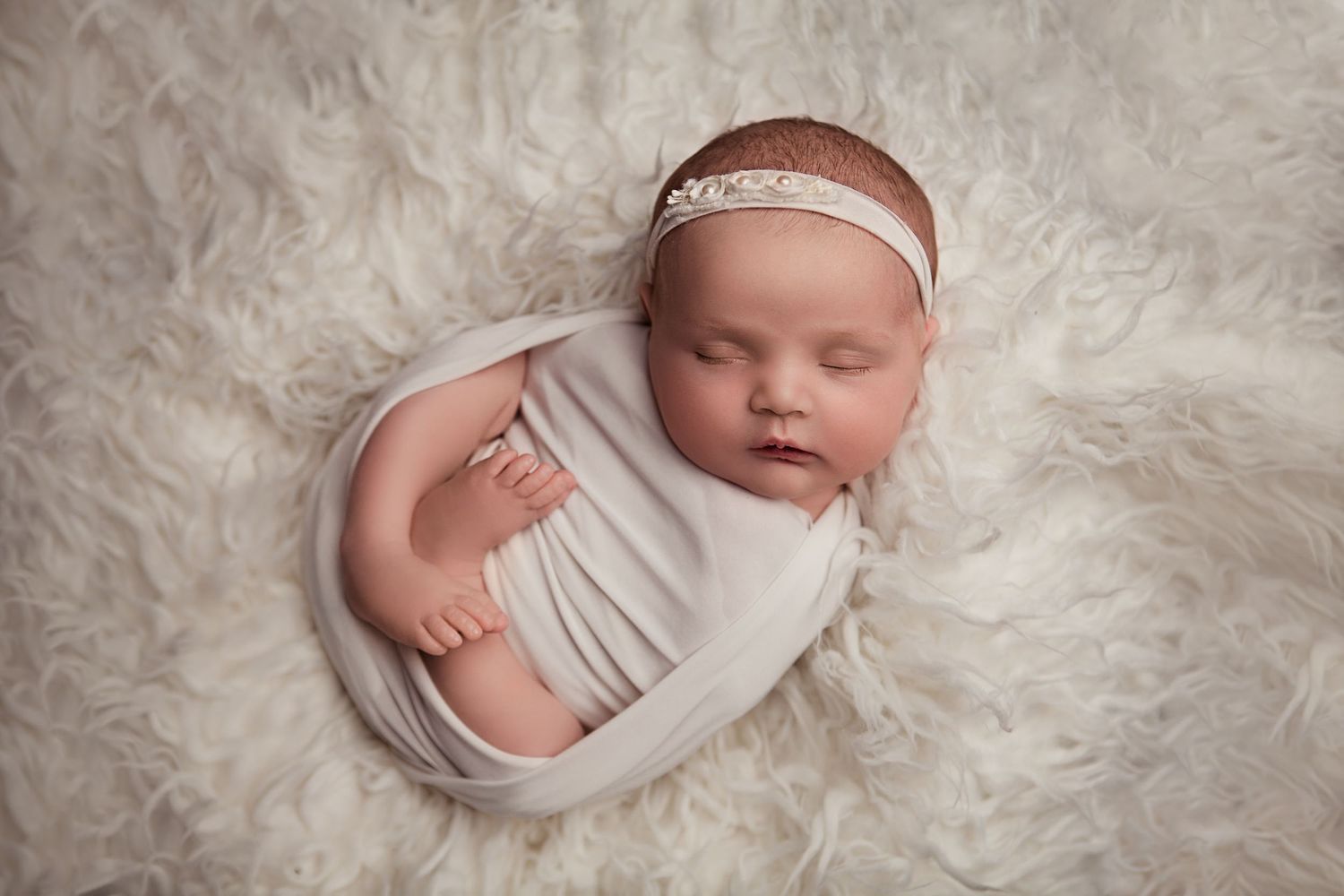 Newborn baby sleeping wrapped in a neutral blanket during a newborn photography session