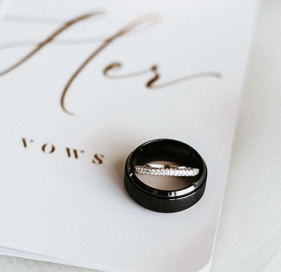 A close-up shot of an elegant black groom's wedding band resting on top of a white 