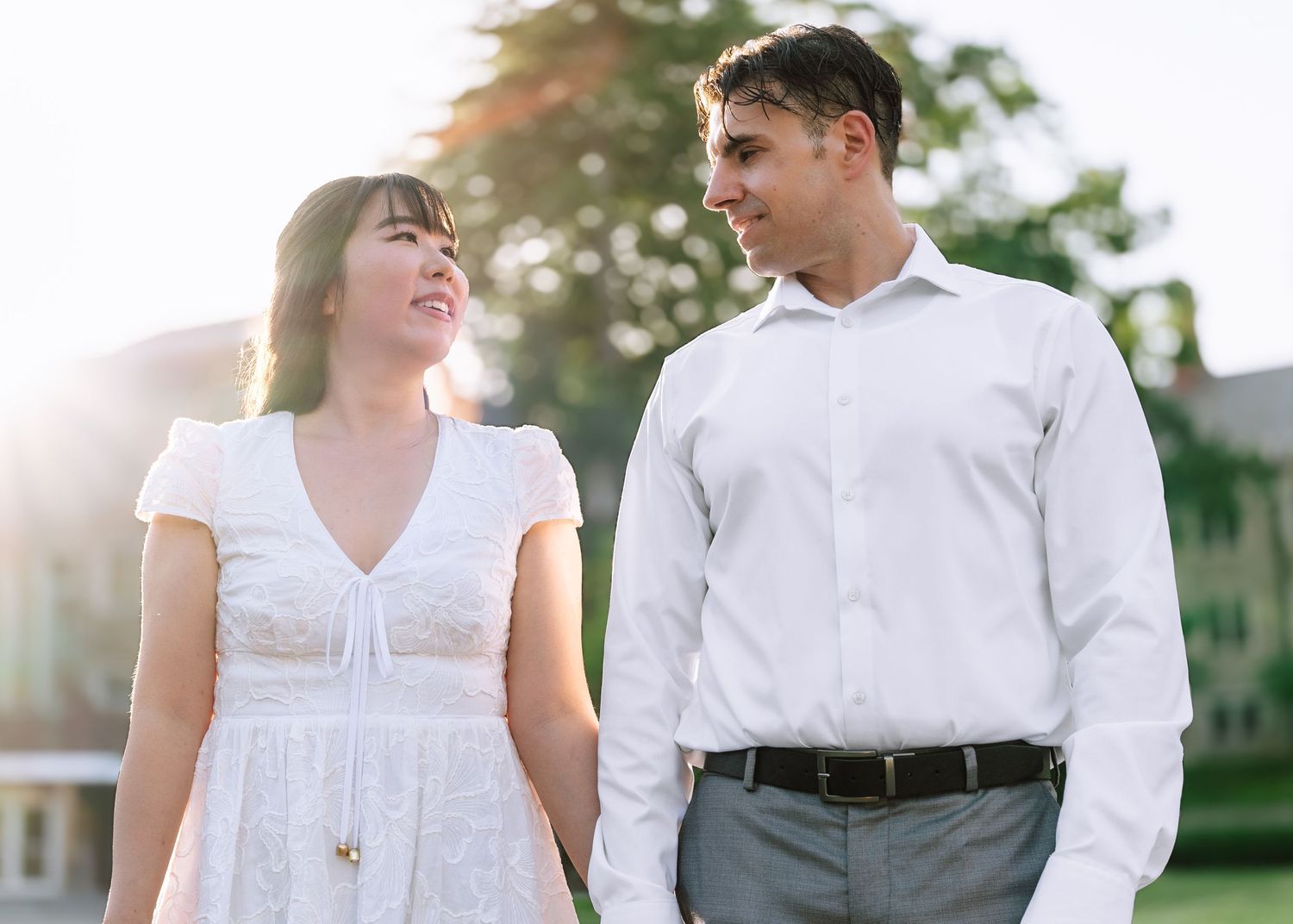 An engaged couple holding hands and walking along a stone path in front of a historic gothic-style building at Princeton University.