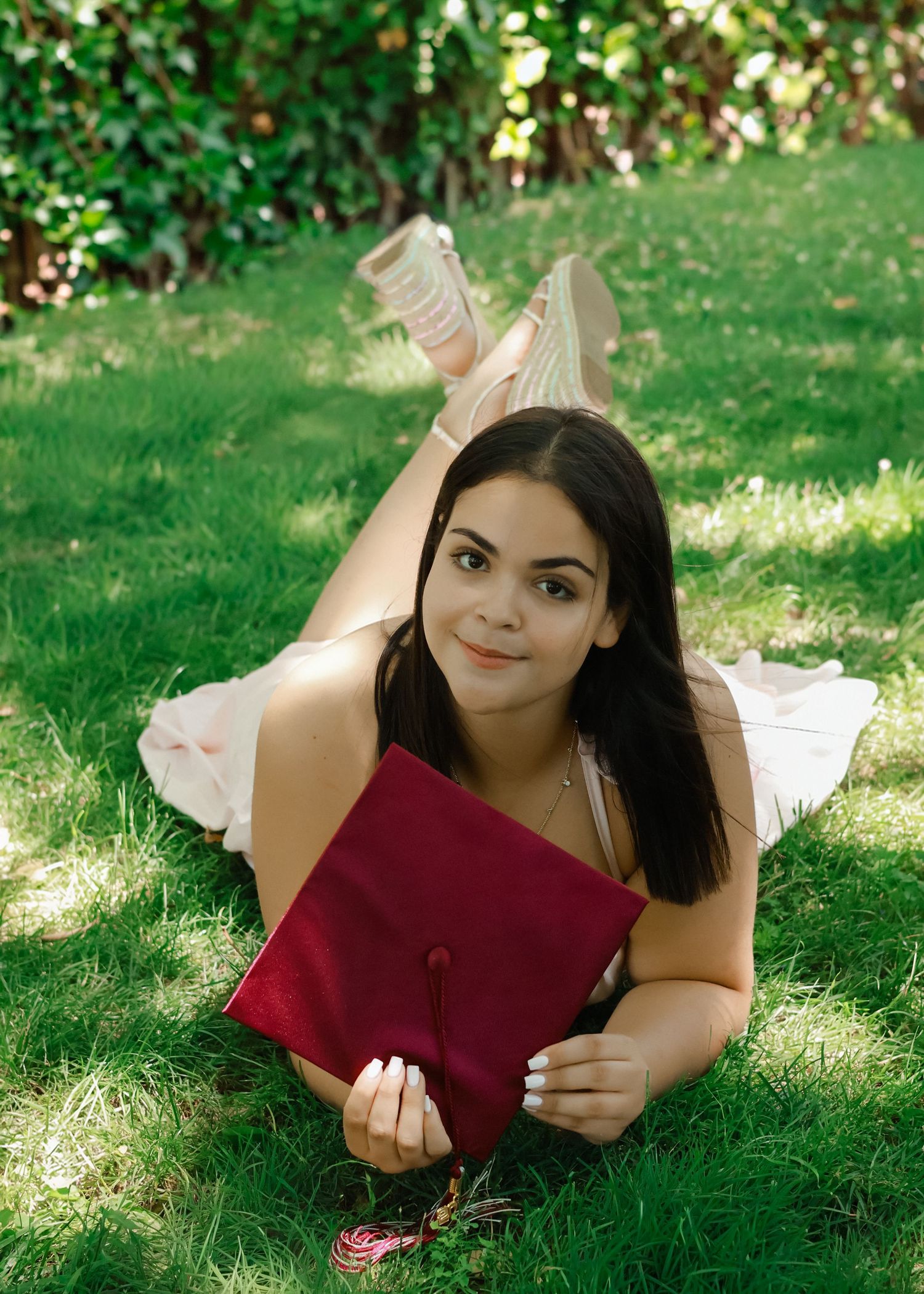 A high school graduate in a light pink dress smiling and holding a graduation pennant while posing next to a classic stone column at Princet