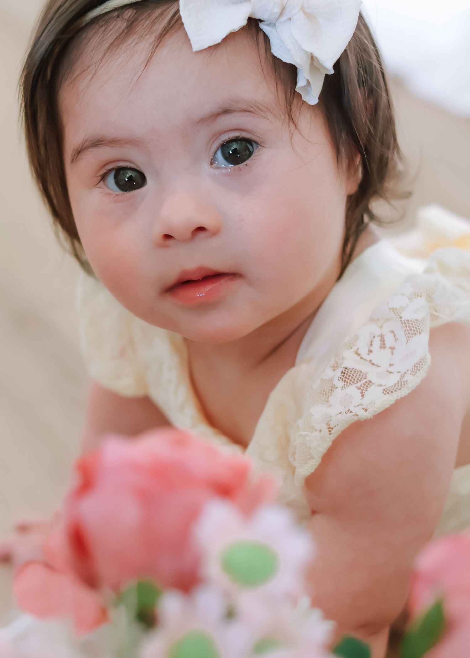 A baby girl celebrating her first birthday, wearing a white tulle dress and sitting on a blanket outdoors in a studio indoors.