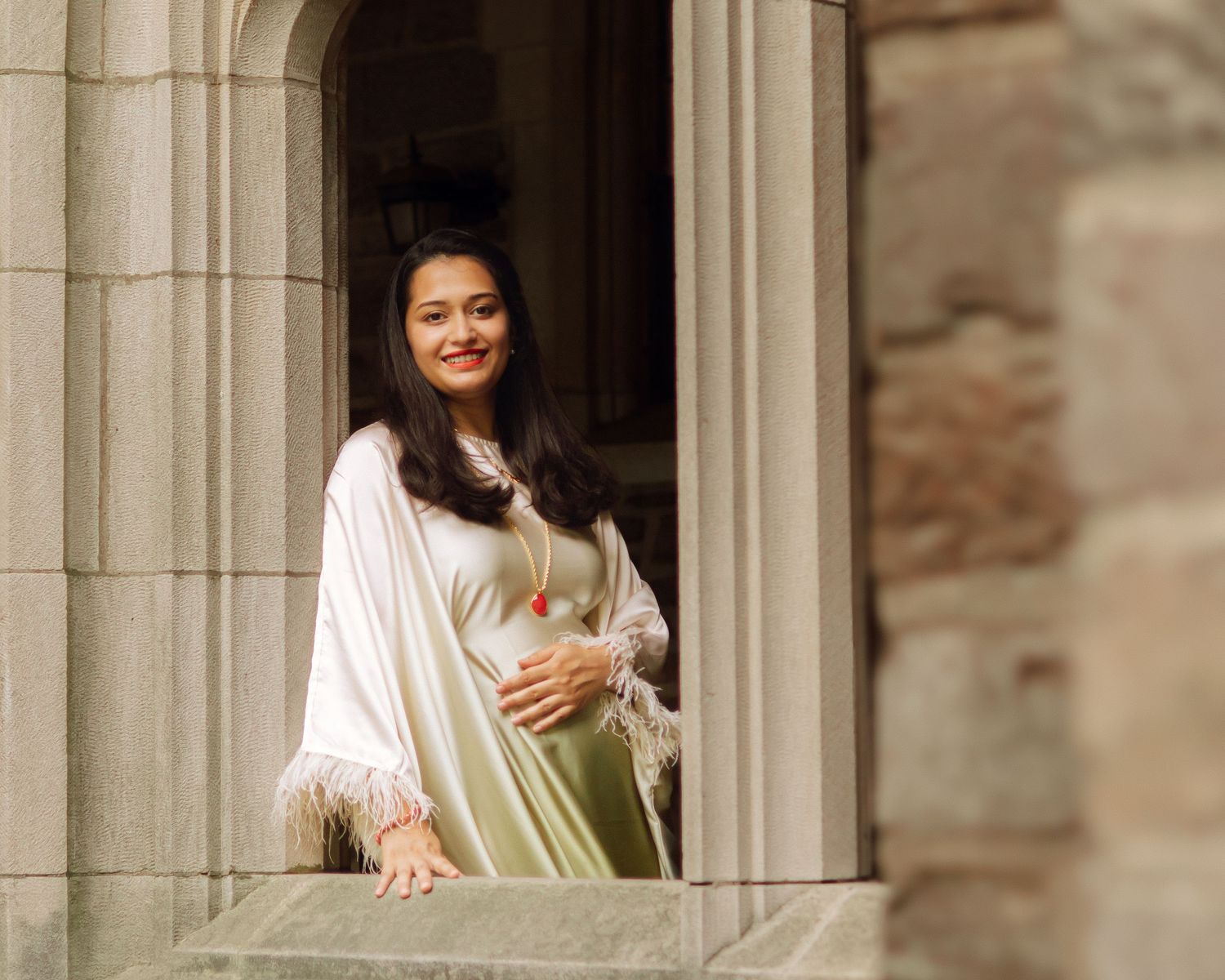 A woman smiling and posing gracefully while leaning against a historic stone gothic window frame at Princeton University in New Jersey.