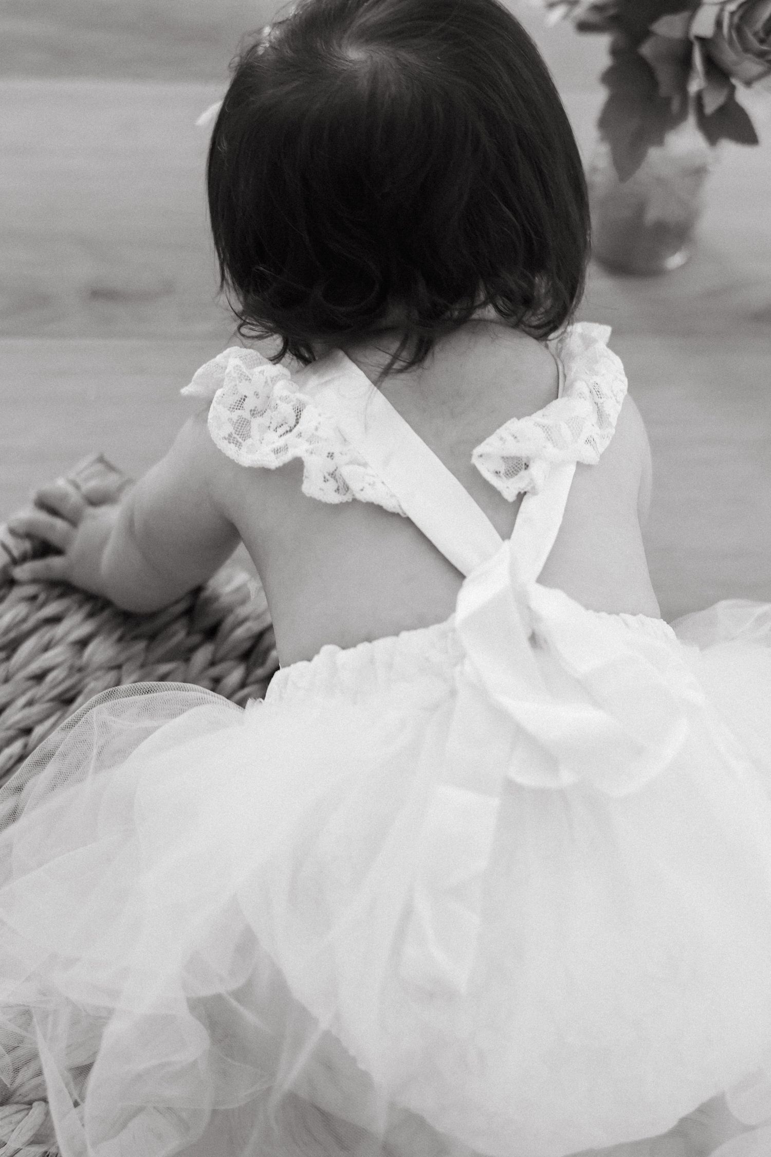A baby girl celebrating her first birthday, wearing a white tulle dress and sitting on a blanket outdoors in a studio indoors.