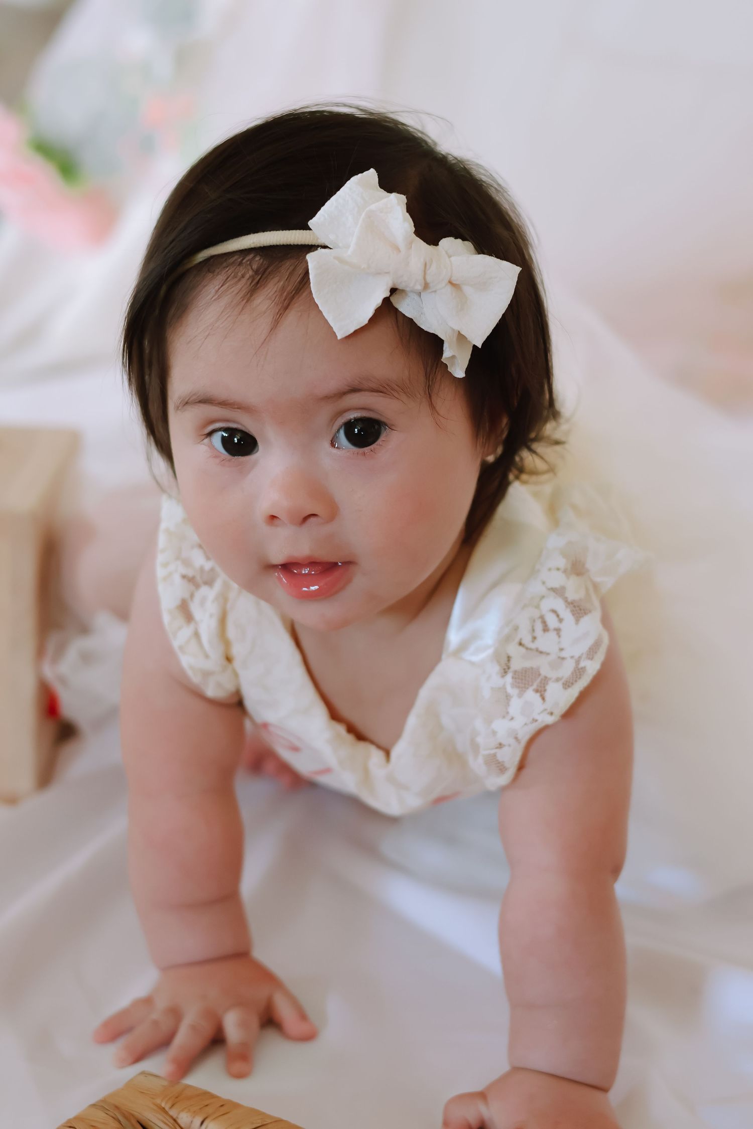 A baby girl celebrating her first birthday, wearing a white tulle dress and sitting on a blanket outdoors in a studio indoors.