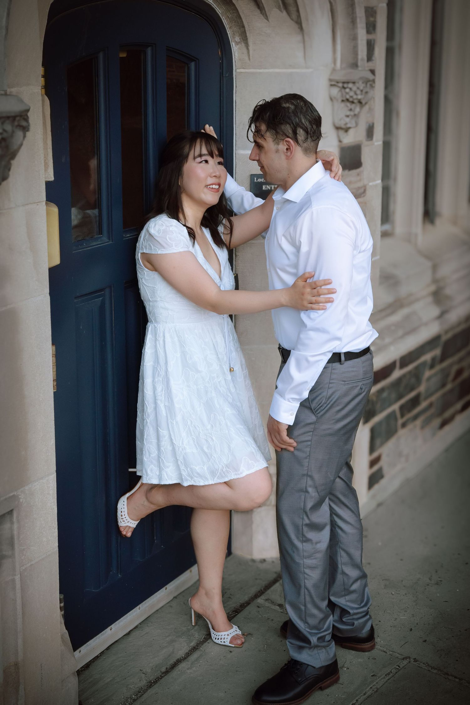 An engaged couple holding hands and walking along a stone path in front of a historic gothic-style building at Princeton University.