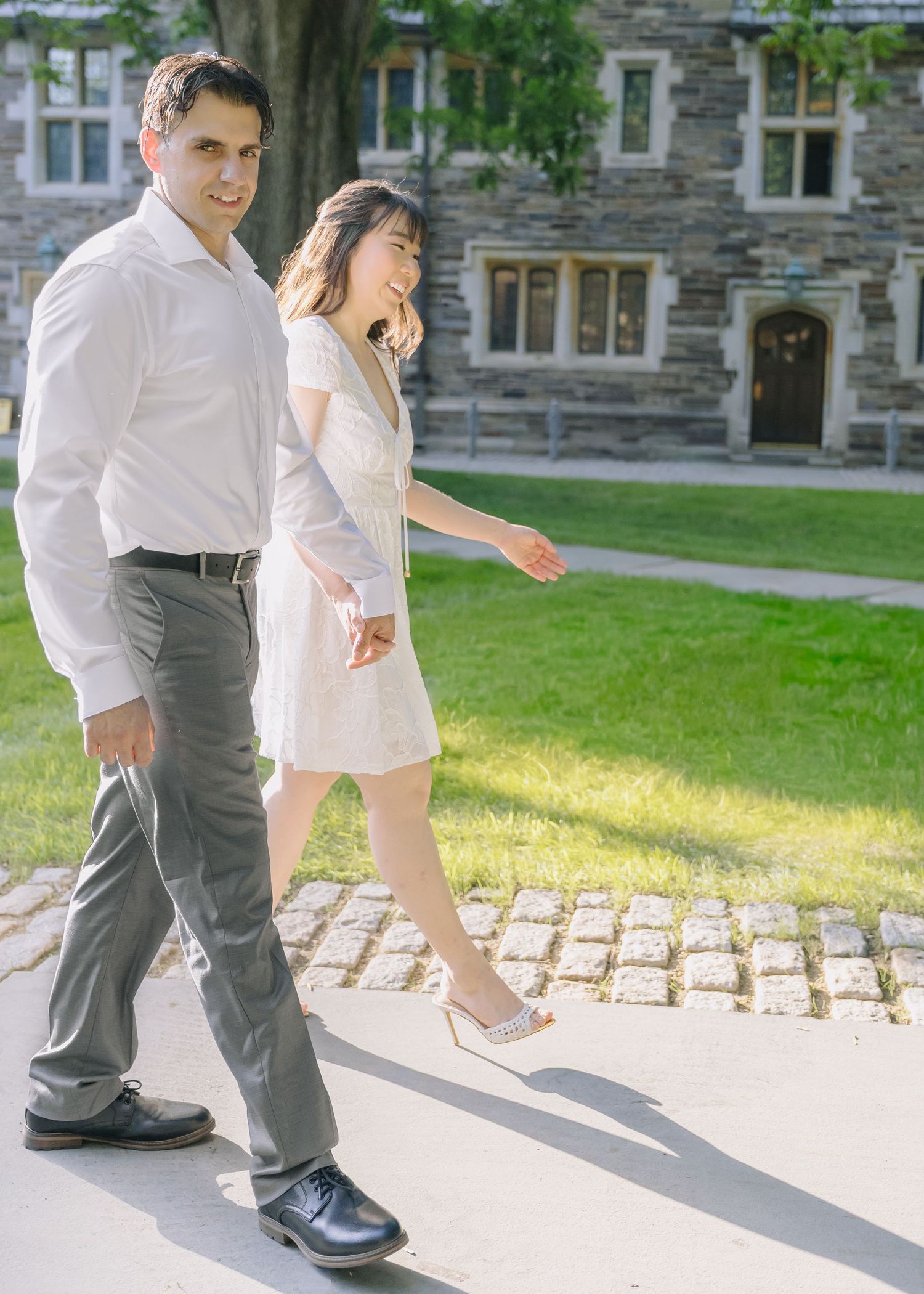 A couple holding hands and smiling while walking near the historic gothic architecture on the Princeton University campus in New Jersey.