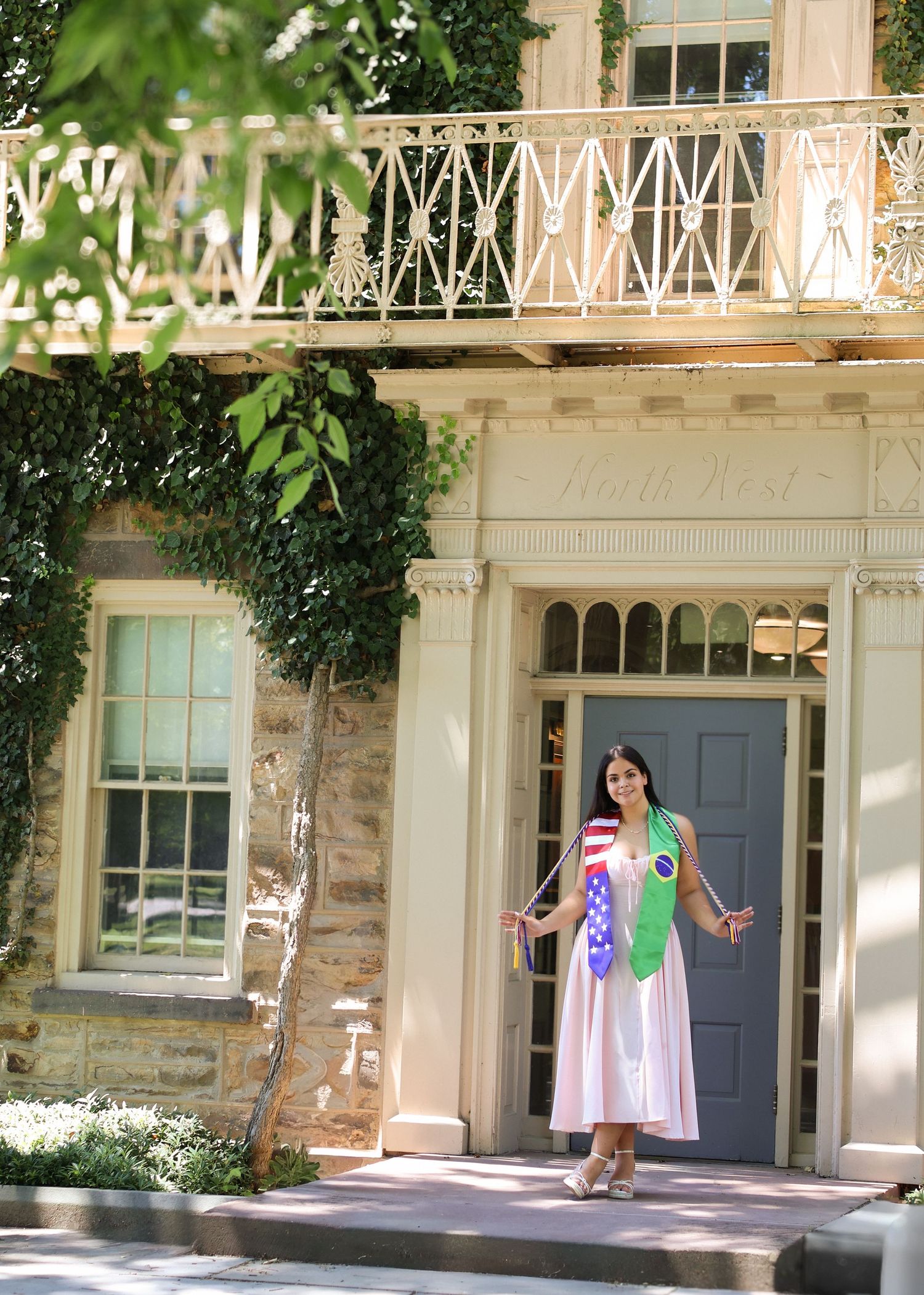A high school graduate in a pink dress smiling and holding a graduation pennant while posing next to a classic stone column in Princeton