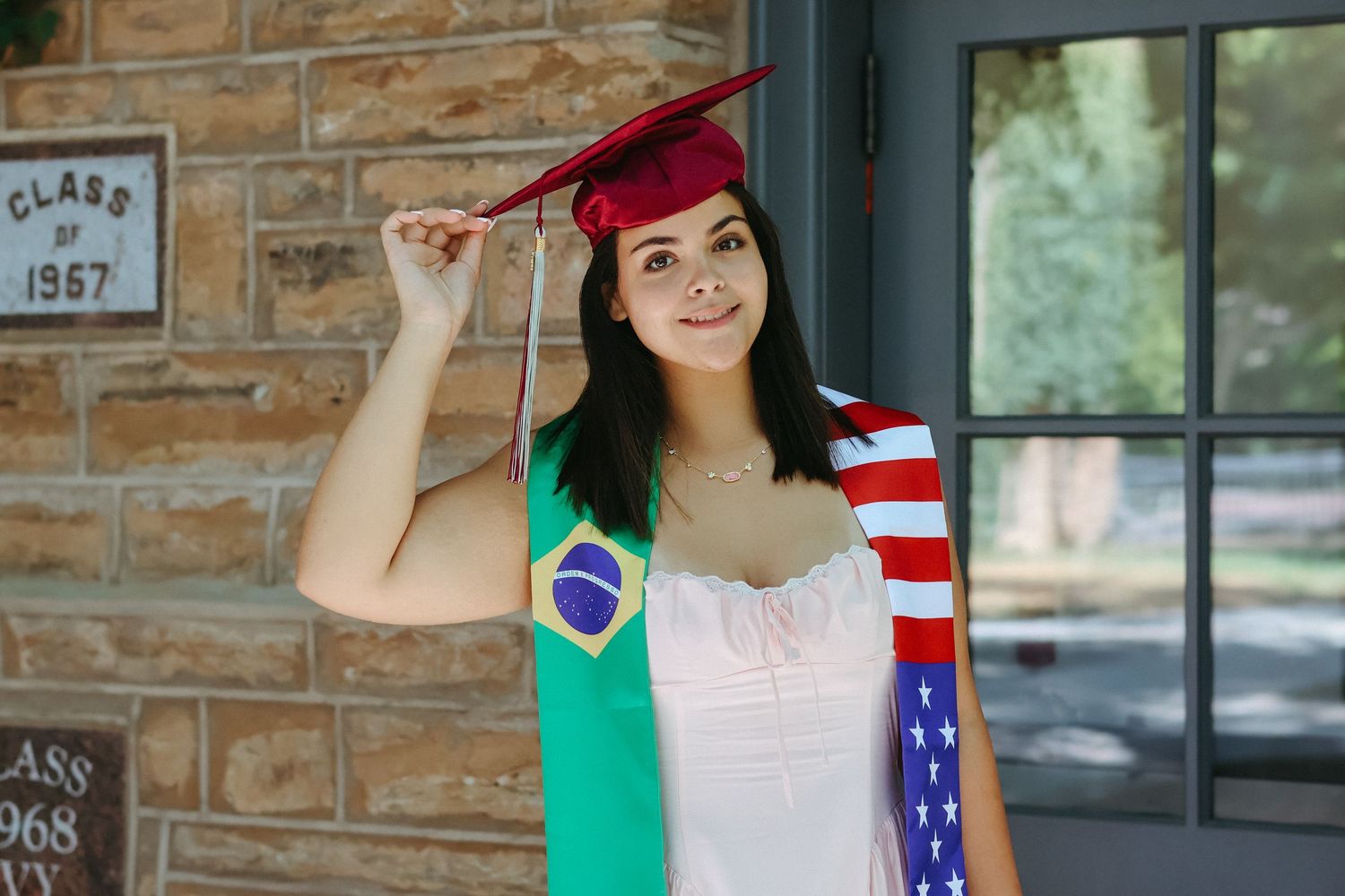 A high school graduate in a pink dress smiling and holding a graduation pennant while posing next to a classic stone column in Princeton