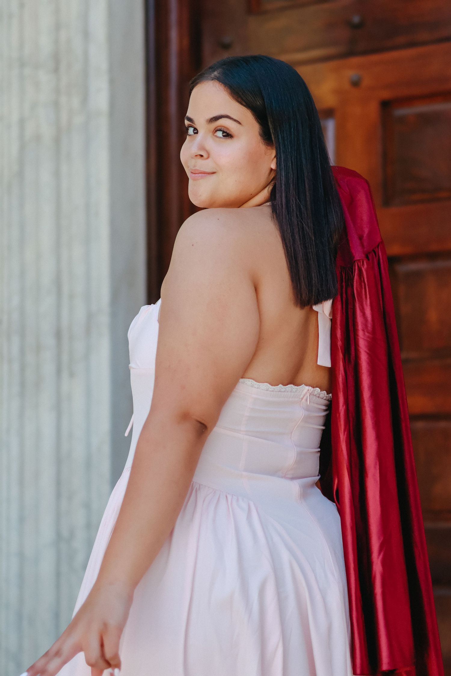 A high school graduate in a pink dress smiling and holding a graduation pennant while posing next to a classic stone column in Princeton