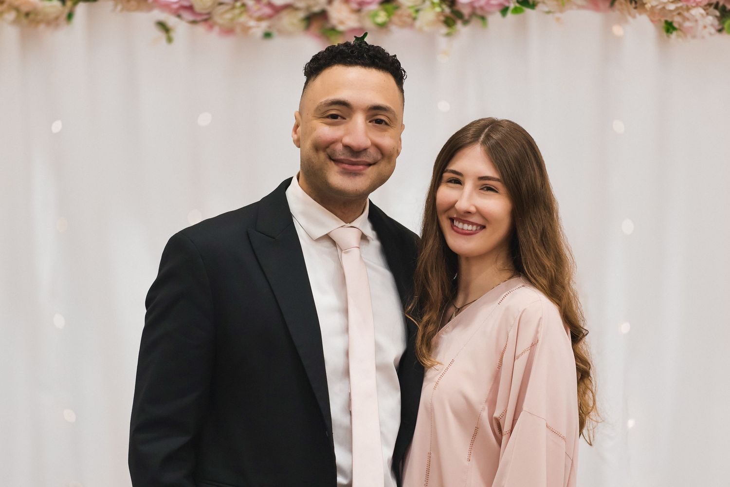 A close-up portrait of a smiling couple in formal wedding attire sharing an intimate moment during an indoor photoshoot.