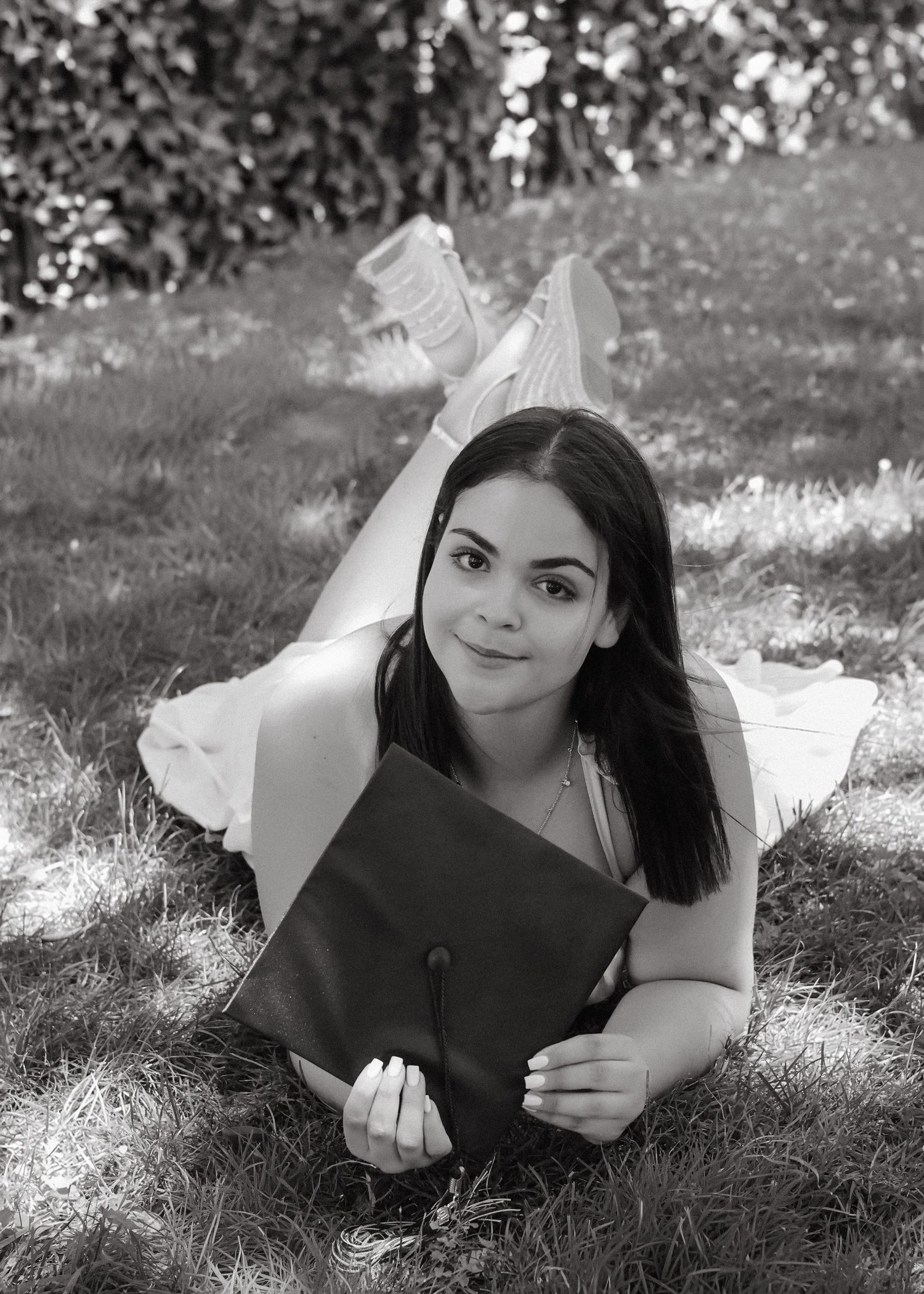 A high school graduate in a pink dress smiling and holding a graduation pennant while posing next to a classic stone column in Princeton