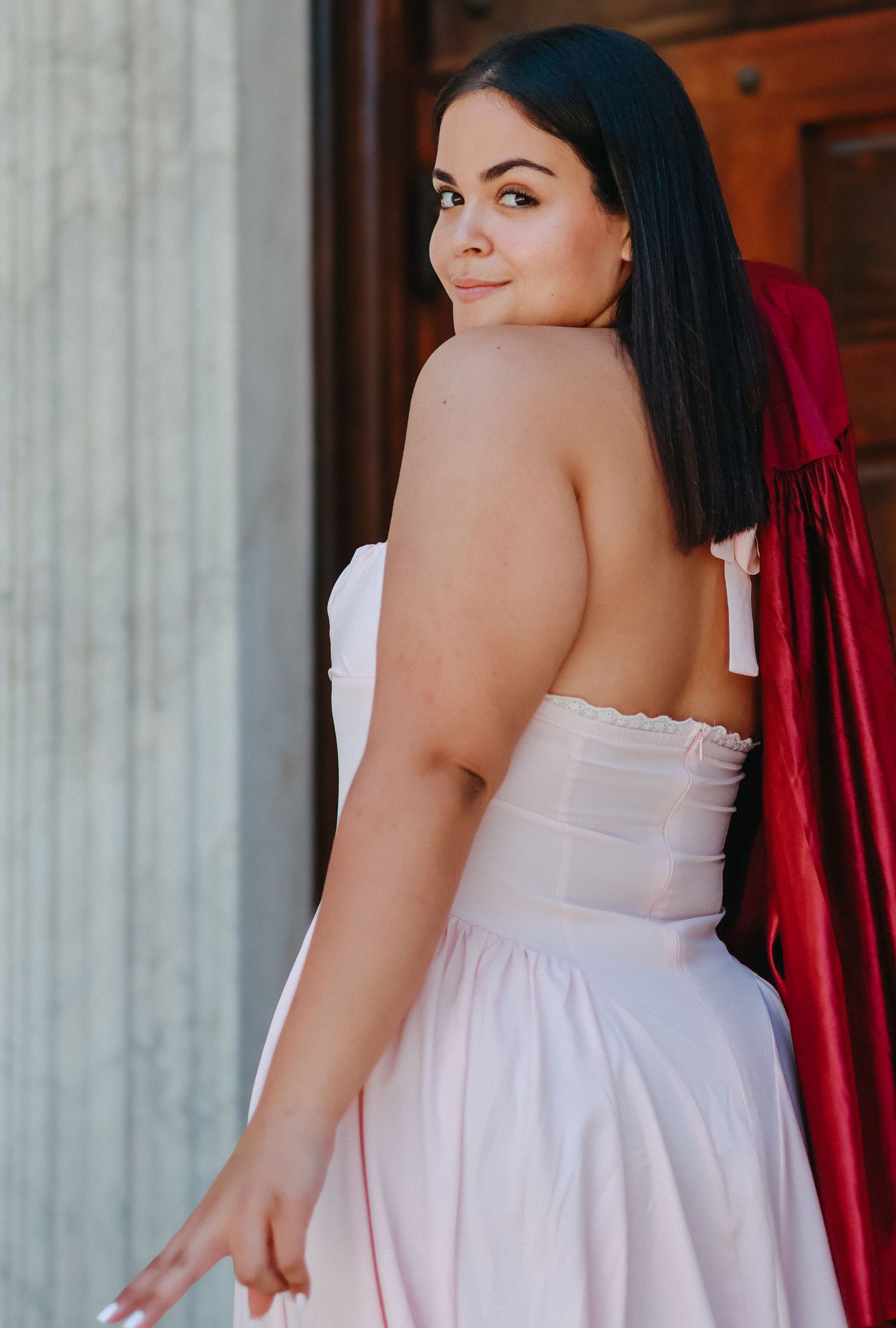 A high school graduate in a pink dress smiling and holding a graduation pennant while posing next to a classic stone column in Princeton