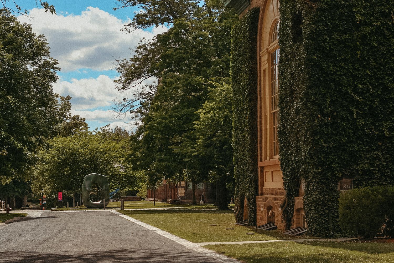 An elegant, ivy-covered brick building at Princeton University, surrounded by lush green trees and a paved walkway under a clear blue sky.