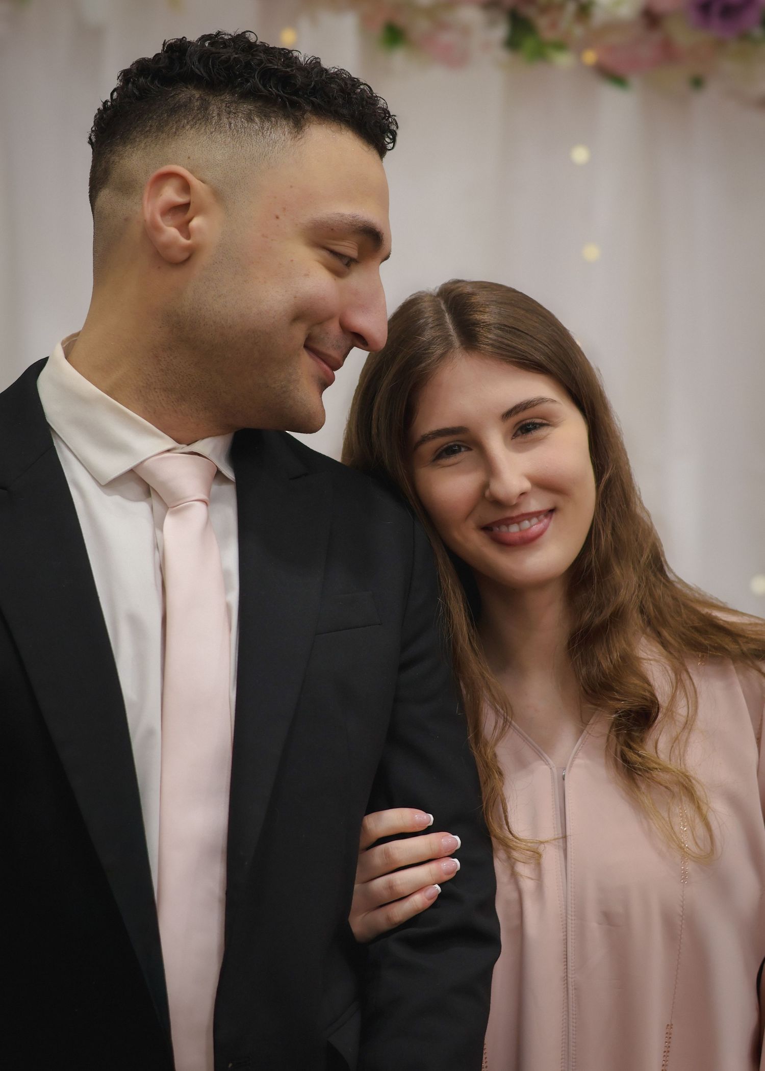 A close-up portrait of a smiling couple in formal wedding attire sharing an intimate moment during an indoor photoshoot.