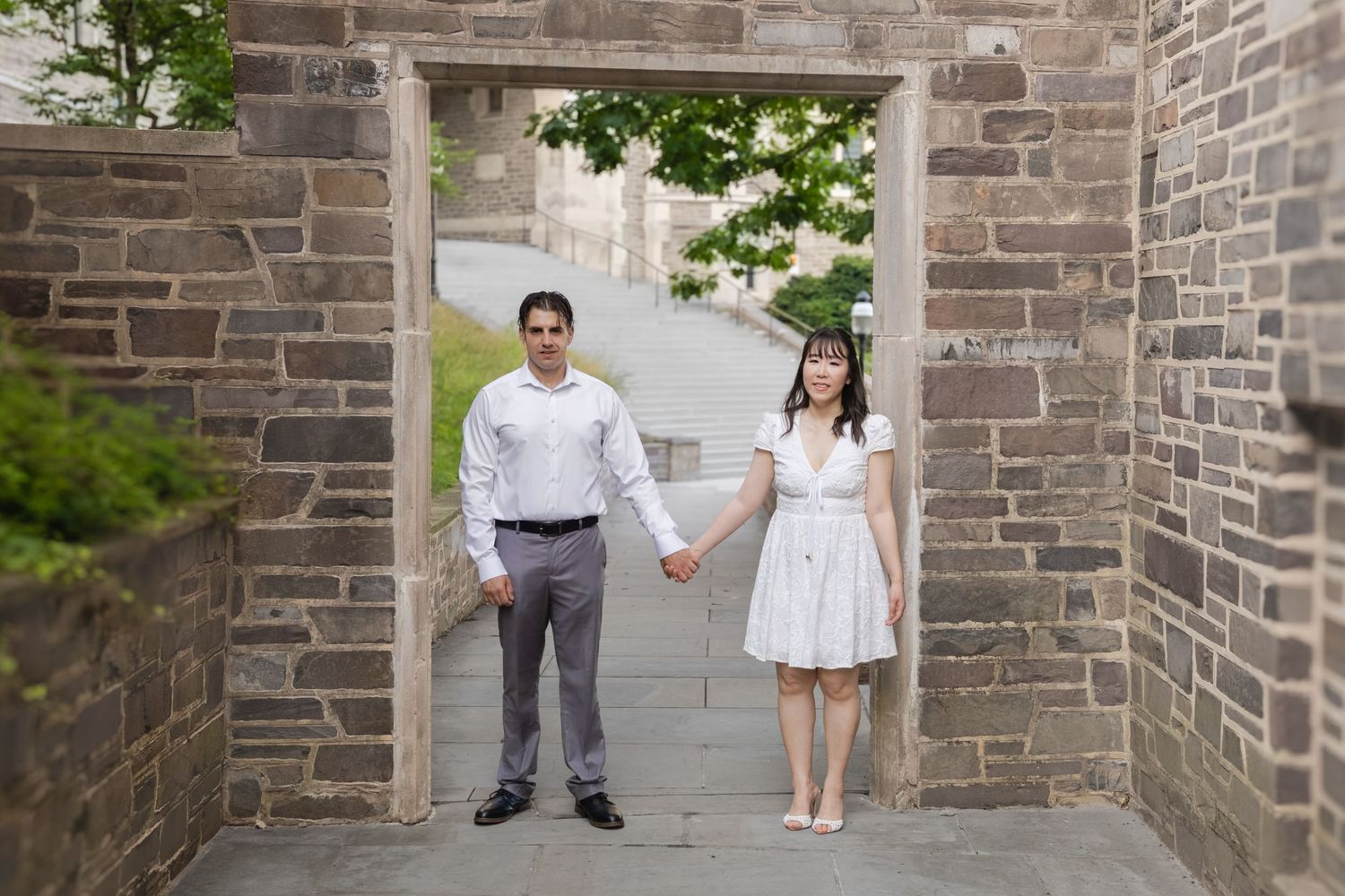 An engaged couple holding hands and walking along a stone path in front of a historic gothic-style building at Princeton University.