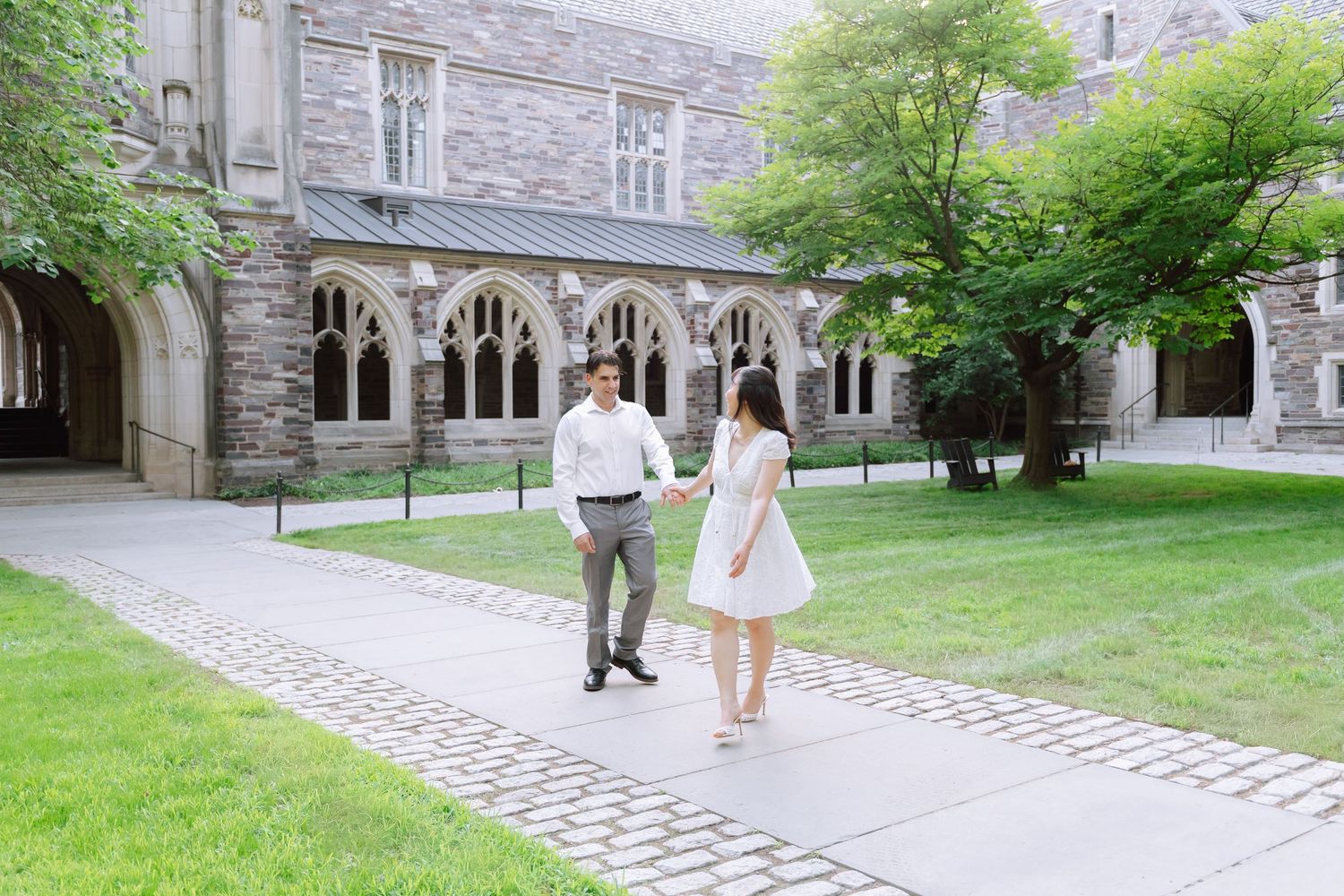 A couple holding hands and smiling while walking near the historic gothic architecture on the Princeton University campus in New Jersey.