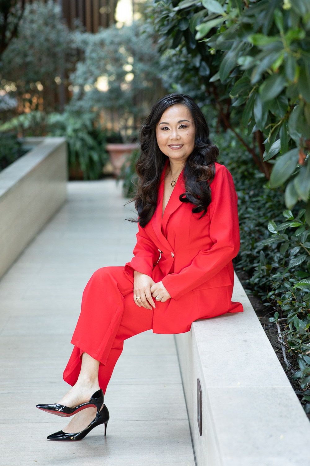 On-location lifestyle portrait of a business woman in a vibrant red jumpsuit sitting outdoors.