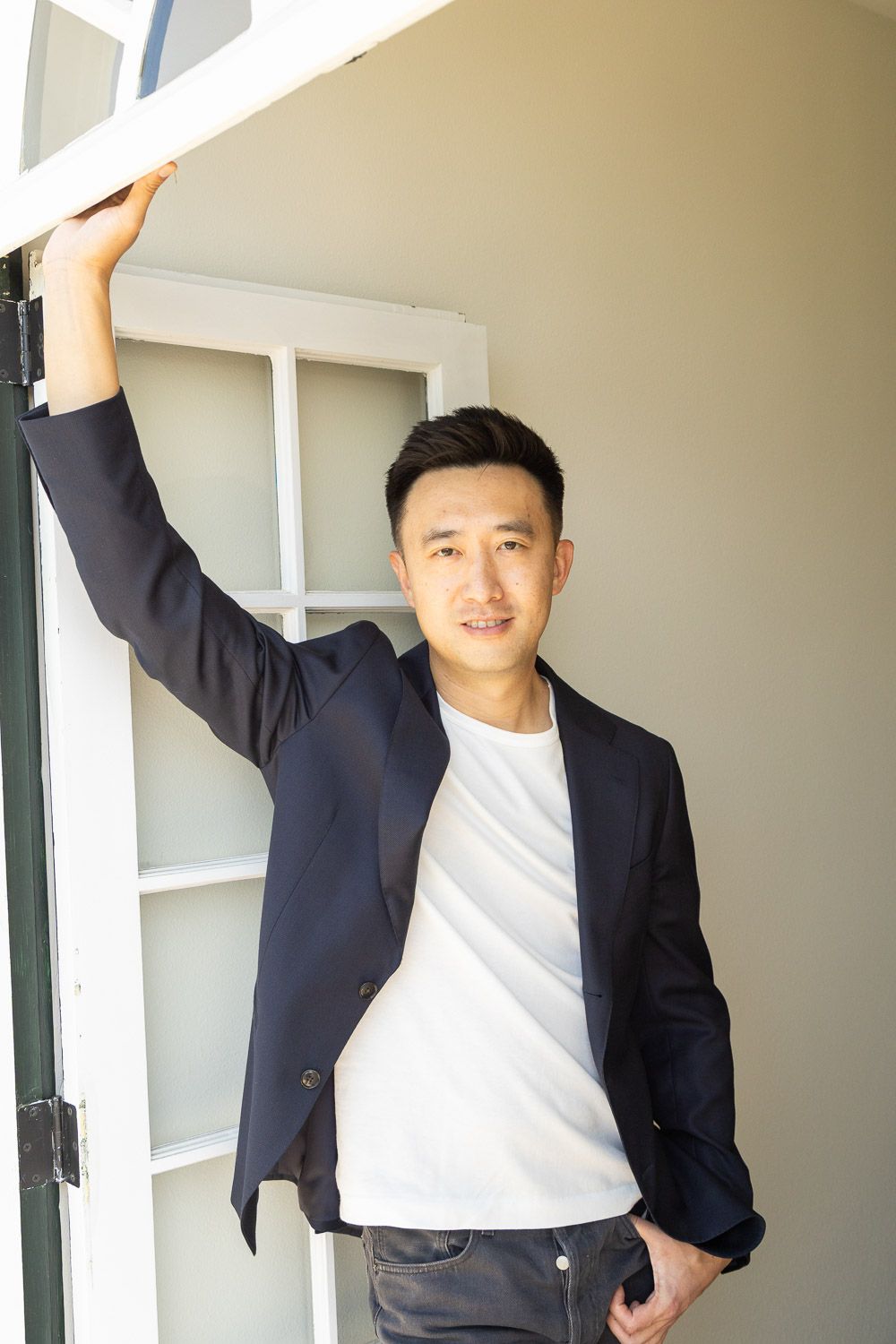 Causal lifestyle portrait of a man leaning in a sunlit in an entryway.