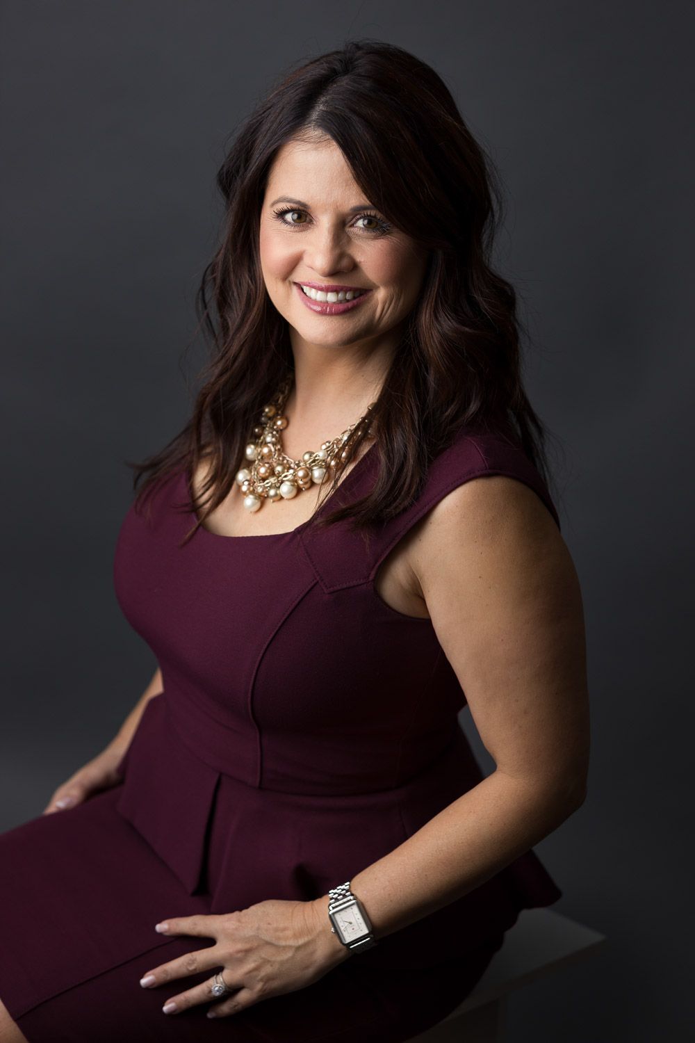 Classic low-key studio headshot portrait of a woman in a dark top against a black backdrop.