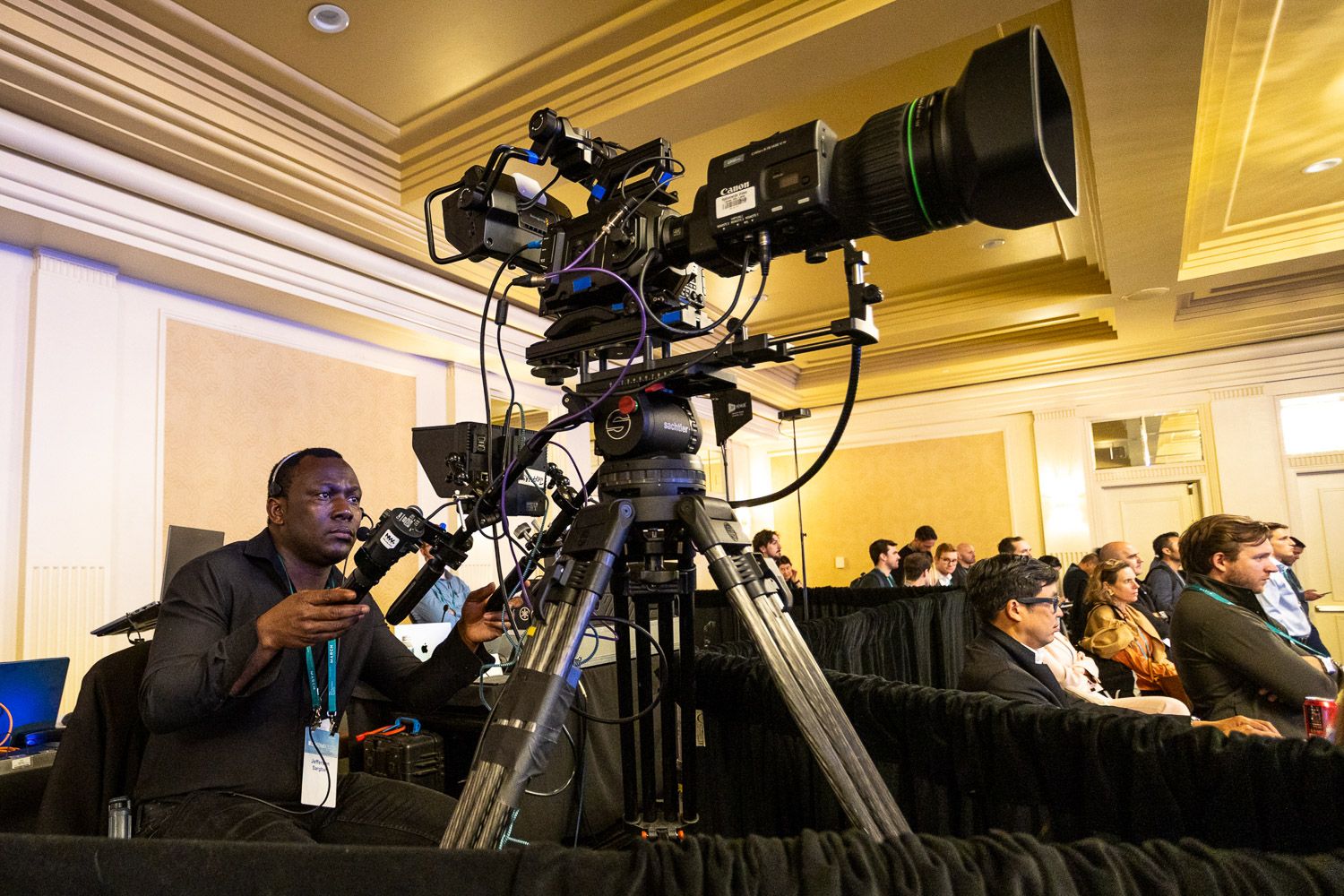 Video camera operator filming a keynote speaker presentation at a formal gala.