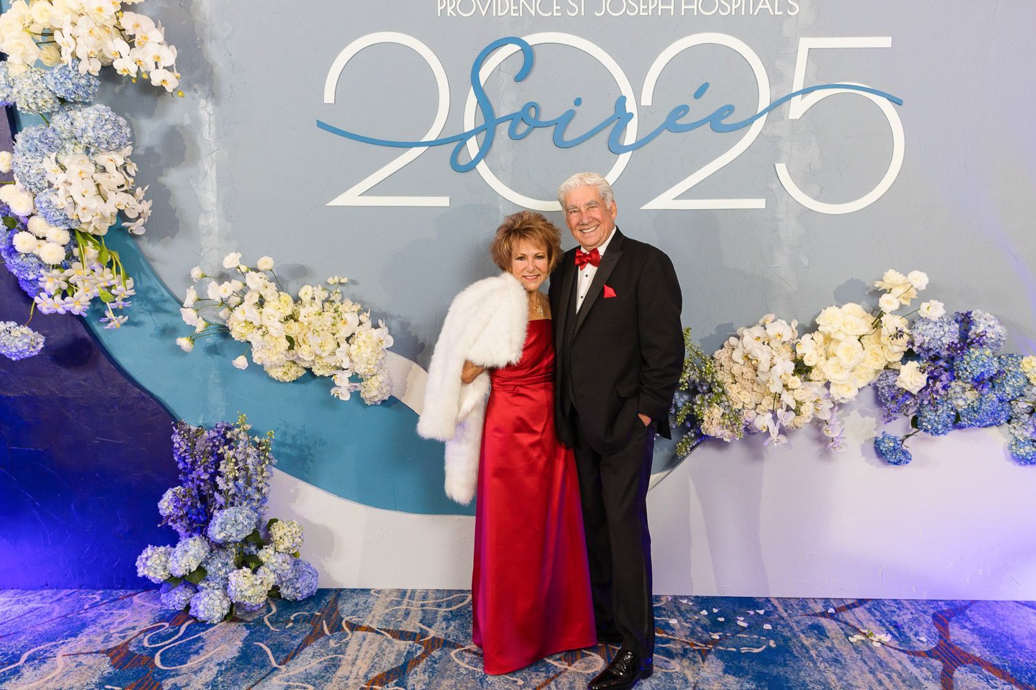 Guests posing at a step and repeat decorated with fresh flowers at a Gala event.