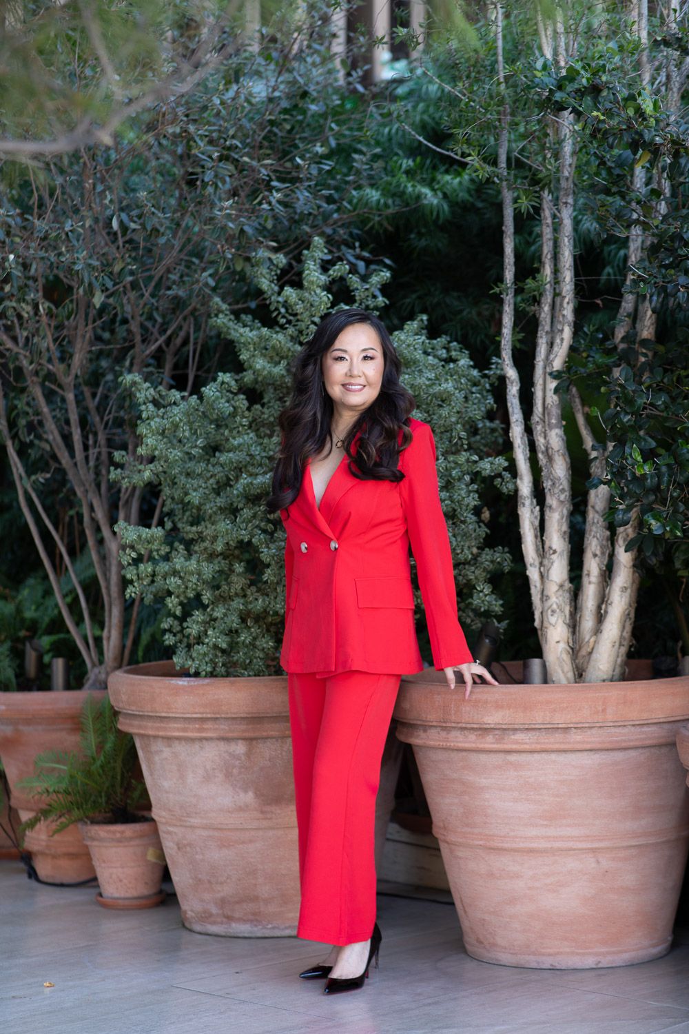 Full-length outdoor professional lifesyle portrait of a woman wearing a red suit.
