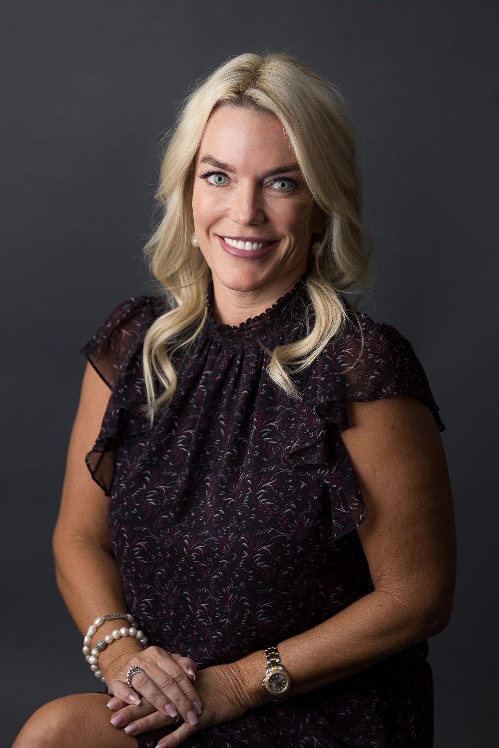 Classic professional studio headshot portrait of a blond woman wearing a black sleeveless top.