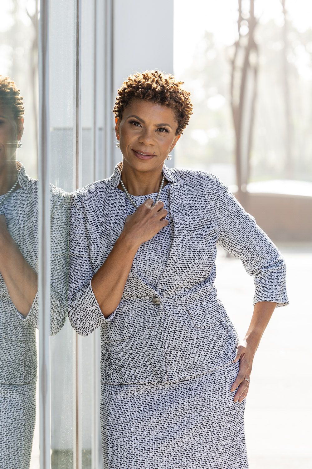 Professional business headshot portrait of a woman leaning against a reflective building.