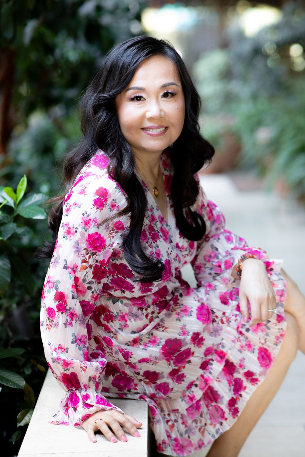 On-location professional portrait of a woment in a floral dress smiling in a courtyard.
