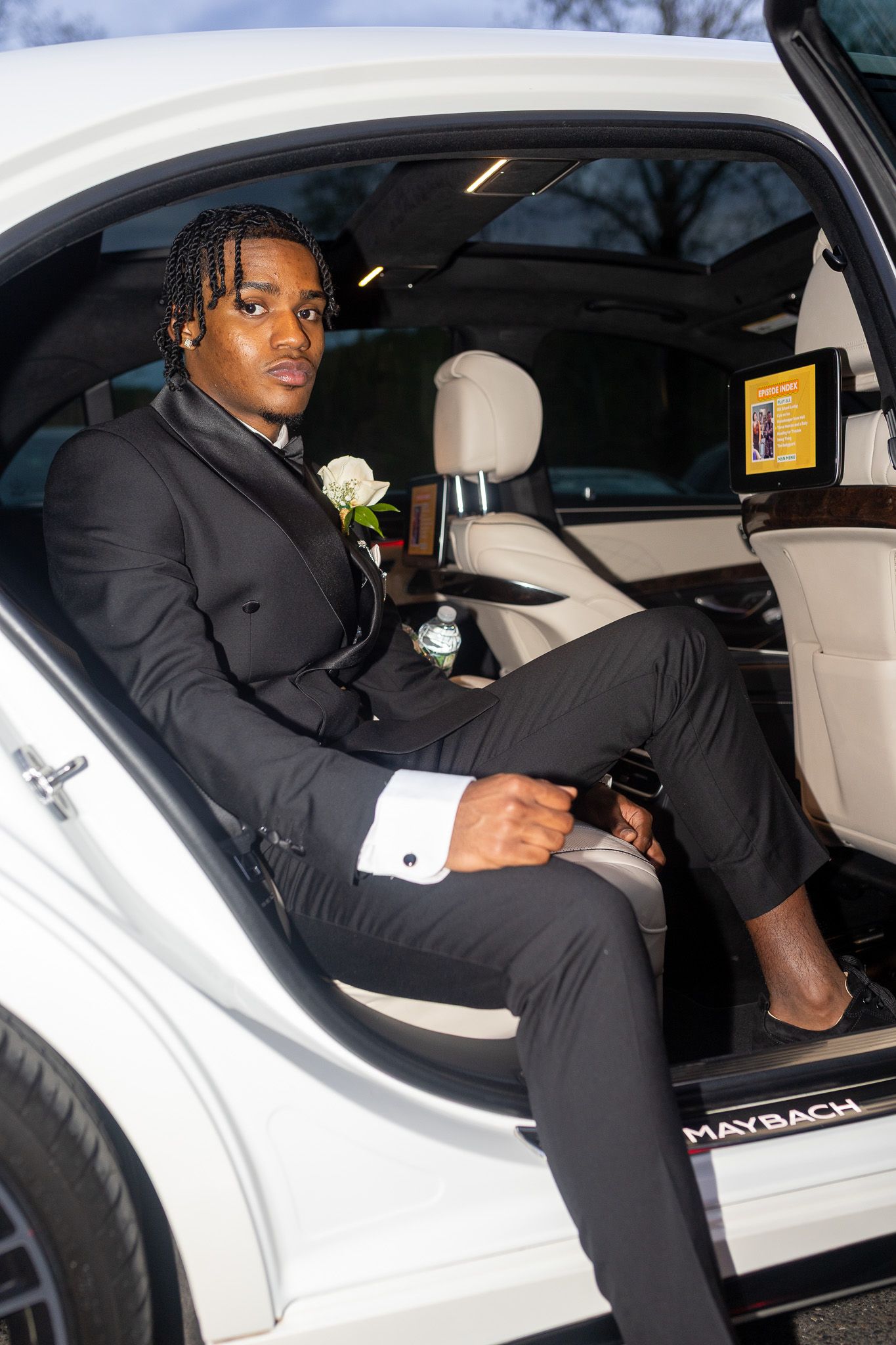 his image features a man in a black suit sitting inside a white Maybach, looking towards the camera. He is preparing for prom.