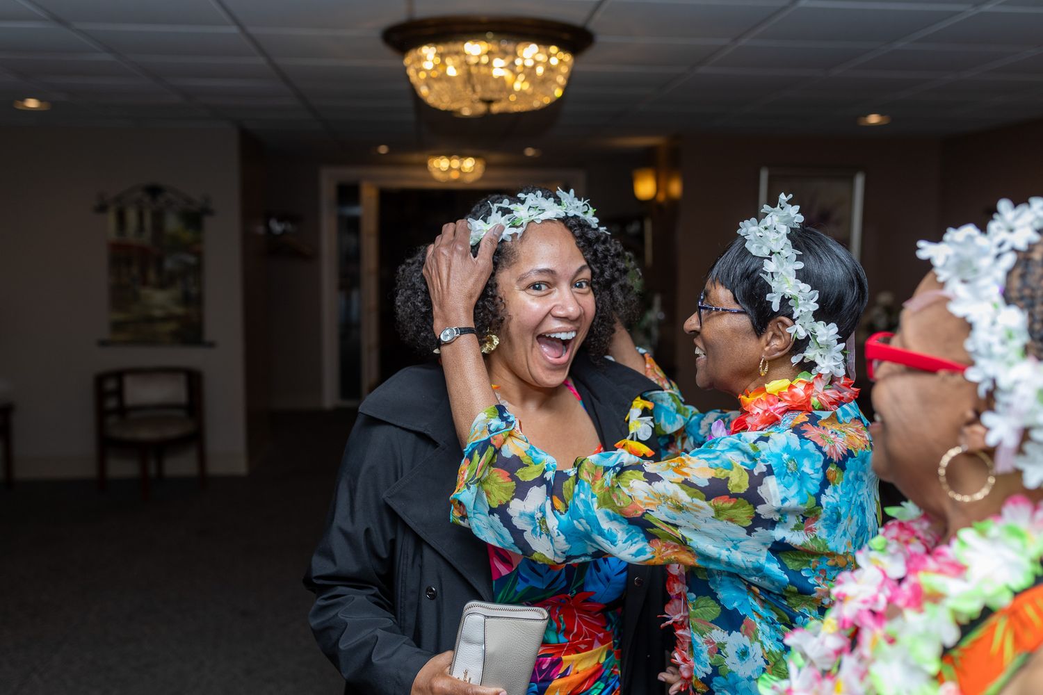 three women celebrating indoors. The woman in the center is wearing a crown and appears to be the guest of honor, possibly for a birthday.
