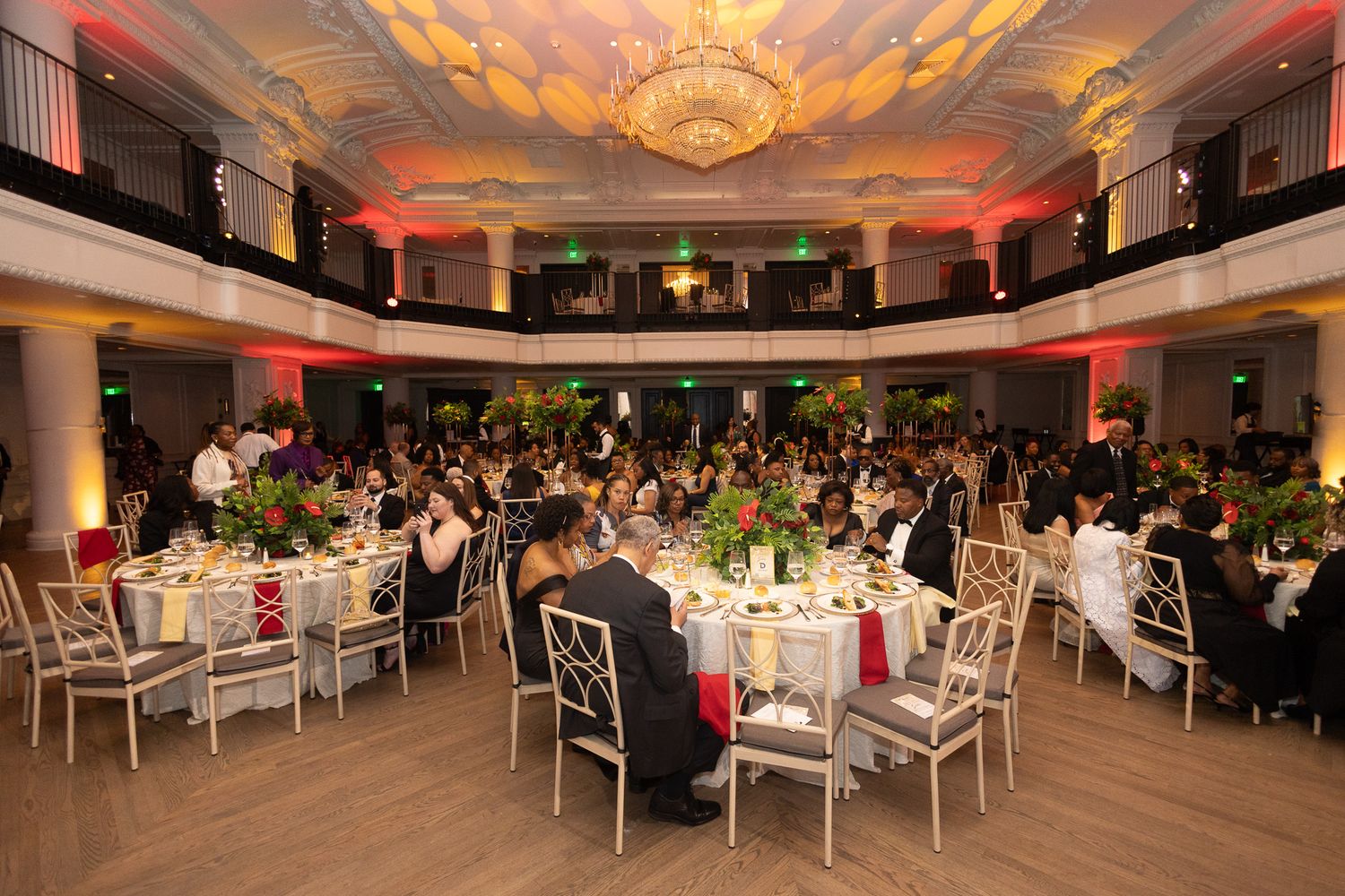 This image features a large, elegant banquet hall filled with round tables set for a formal event. Guests are seated at the tables.
