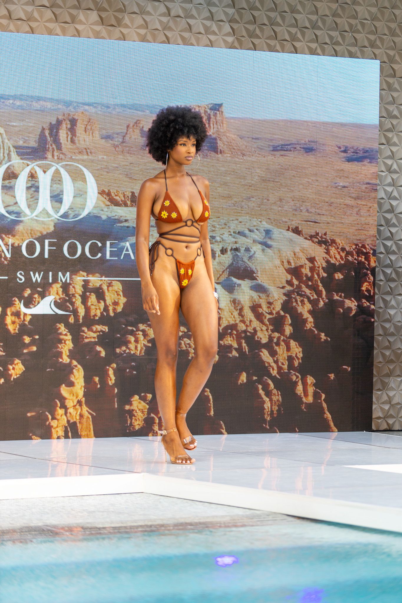 This photo features a model walking down a runway wearing a metallic gold bikini with a matching sheer cover-up.