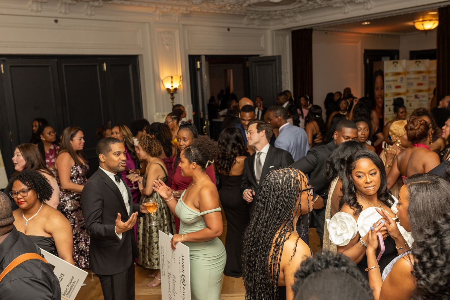 This image features a lively indoor social event or reception with a large group of people mingling and conversing. Guests are dressed.