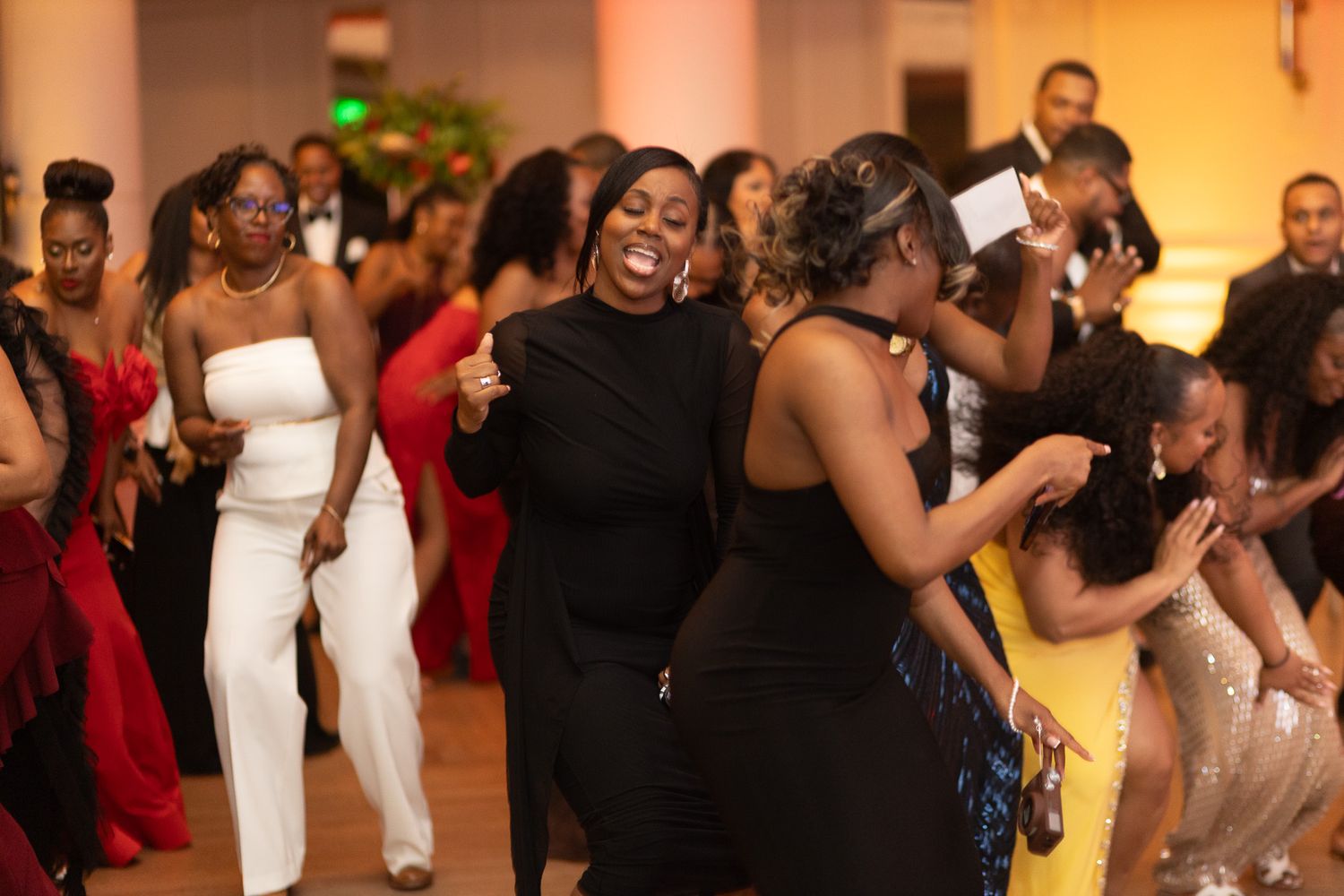 a group of people dancing and celebrating at an indoor event. They are dressed in formal attire, and the atmosphere appears lively.