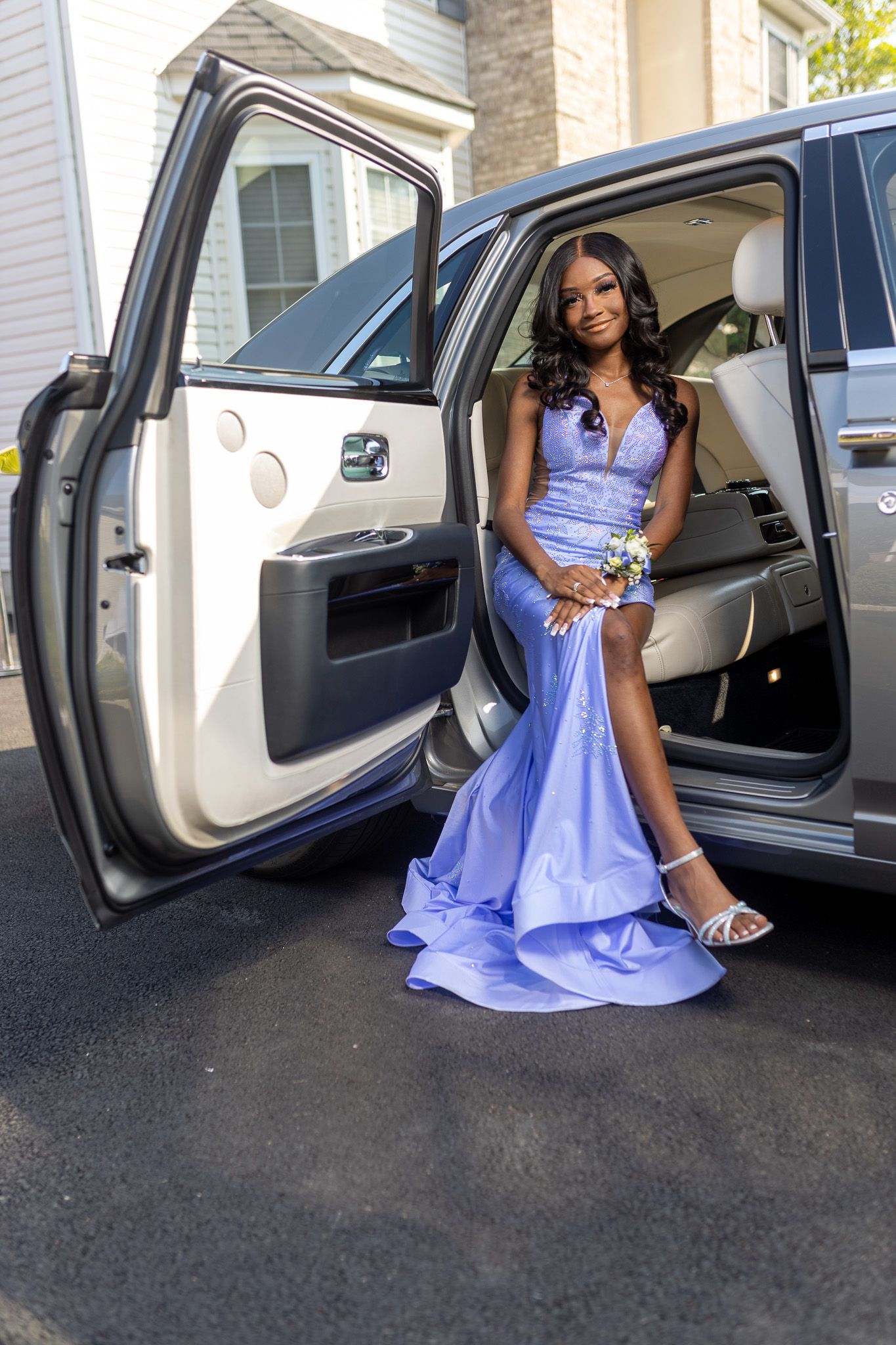 a woman in a long, flowing light blue dress stepping out of the back seat of a Rolls Royce. Wearing silver  heels and purple prom dress.
