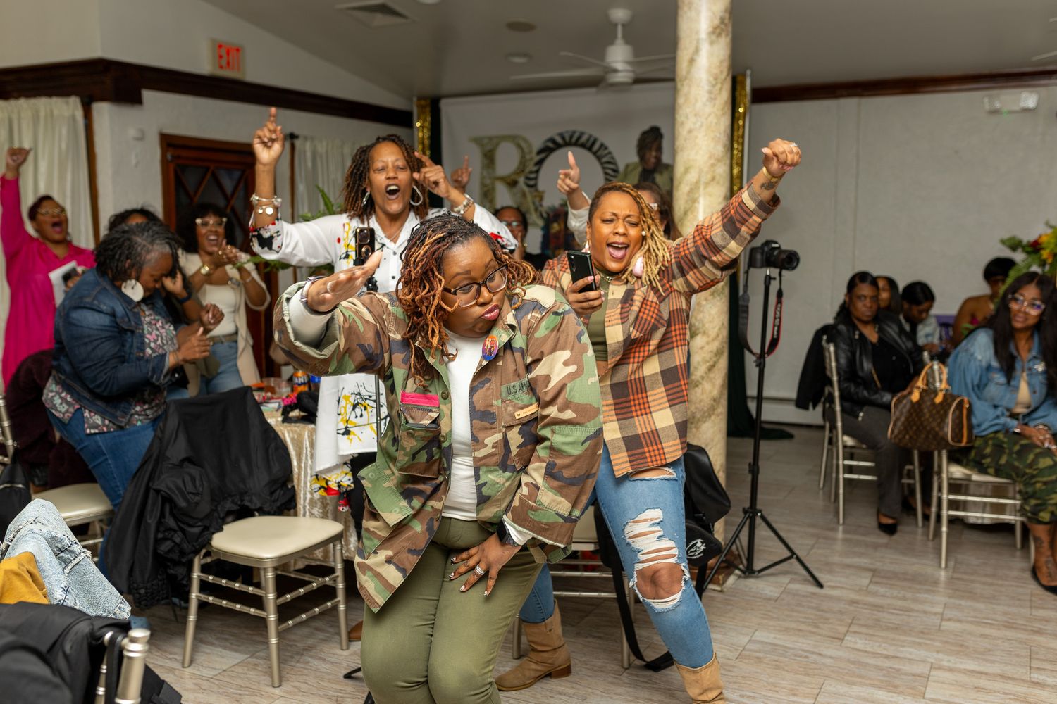 This photo features a group of women posing together indoors, with several of them raising their arms in celebration.