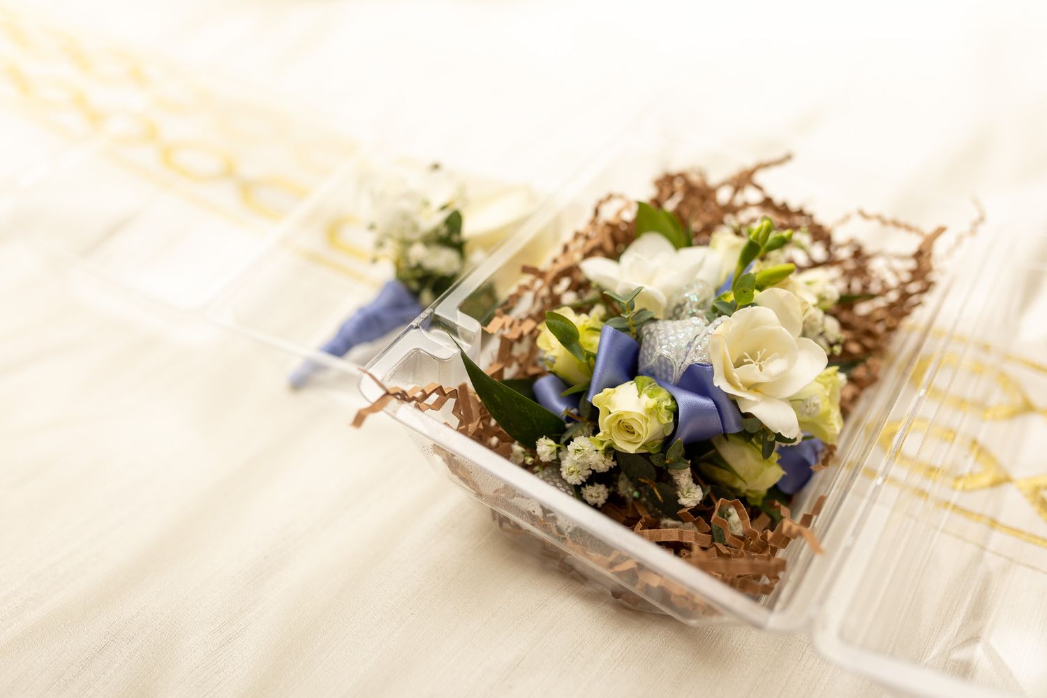 This image features a floral corsage or small arrangement, primarily composed of white and blue flowers, nestled among green foliage.