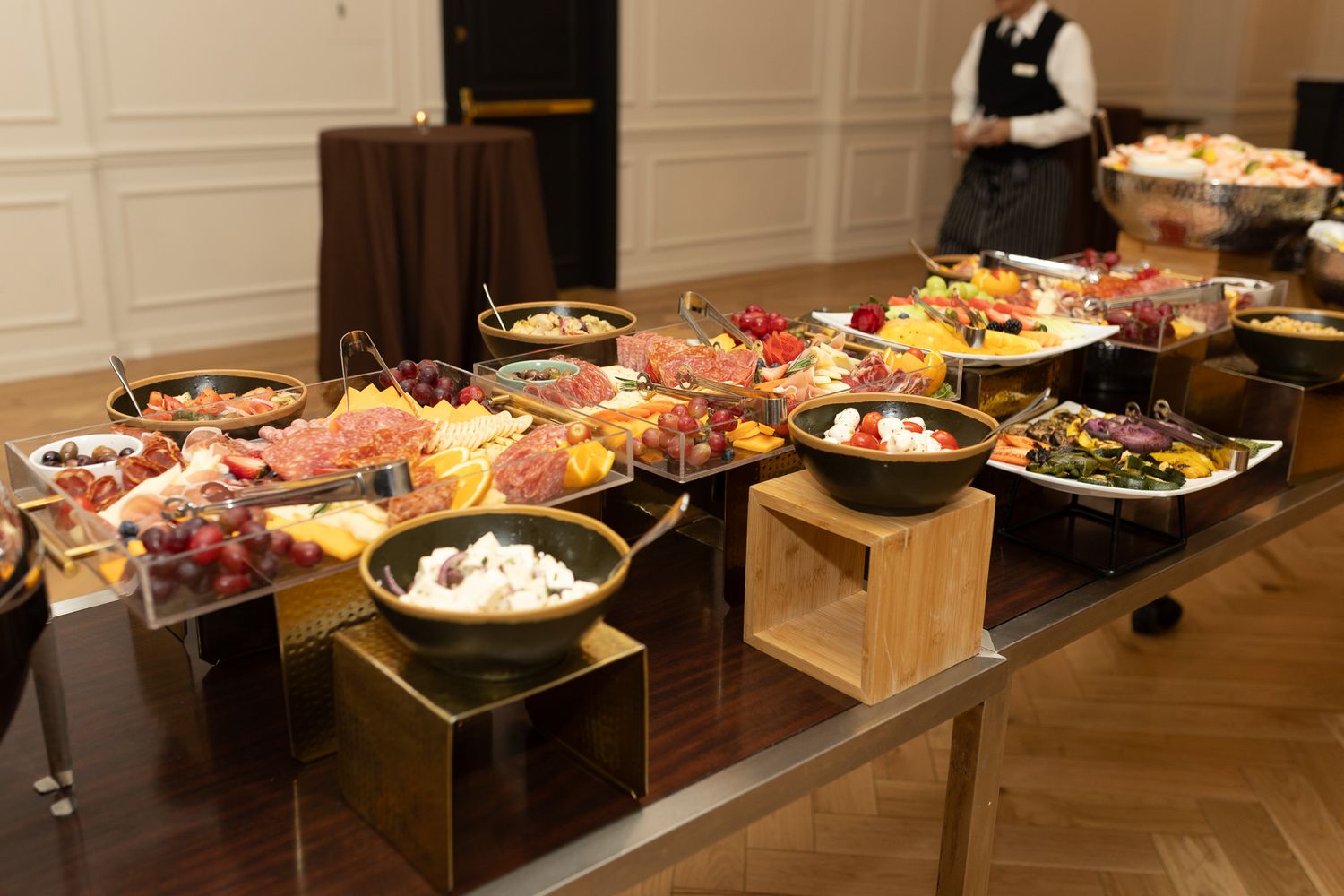 This image shows a buffet table with a variety of food, including charcuterie, fruit, and what appears to be nuts or small snacks in bowls.