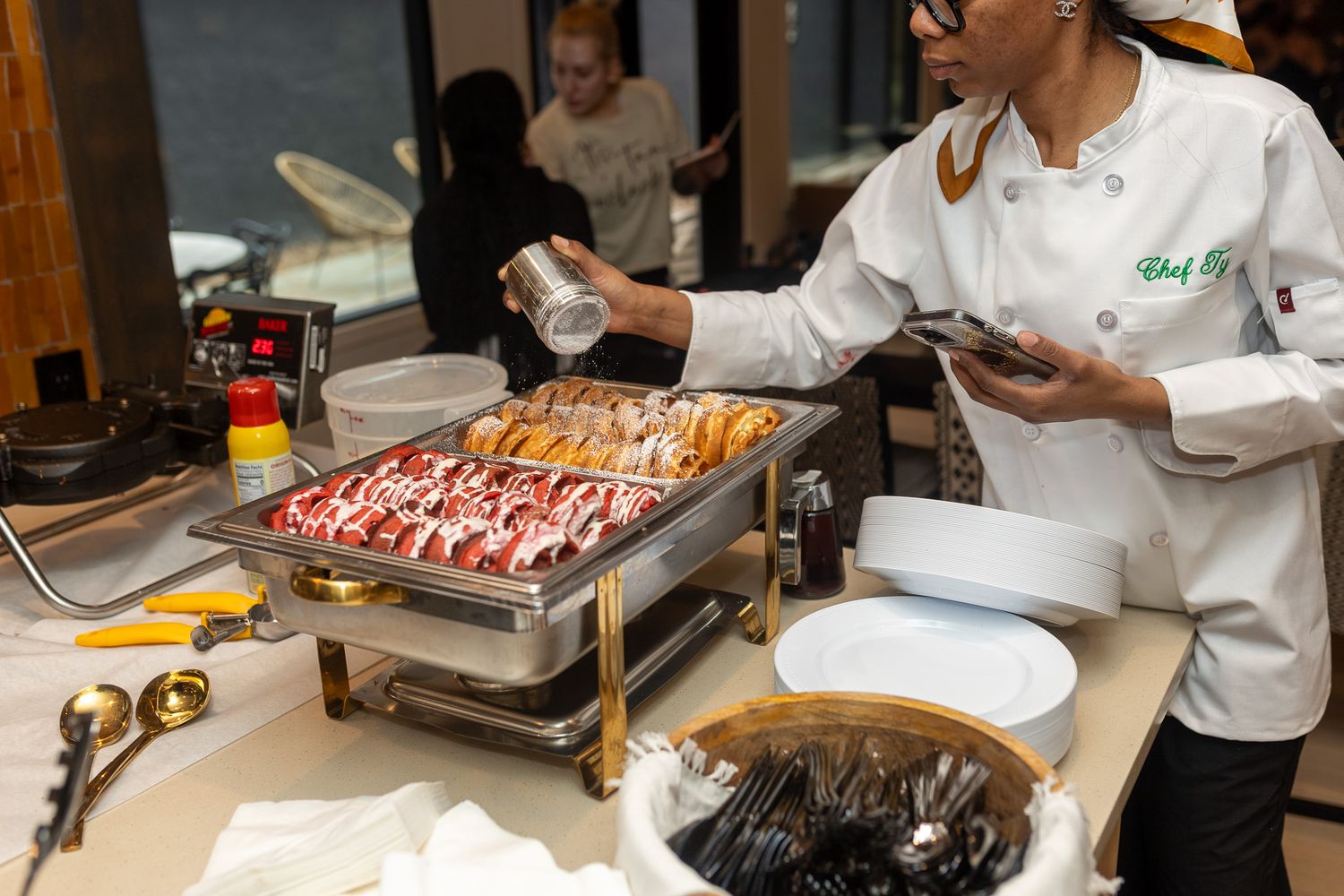 a chef serving food from a buffet, with several chafing dishes containing various dishes laid out on a table.