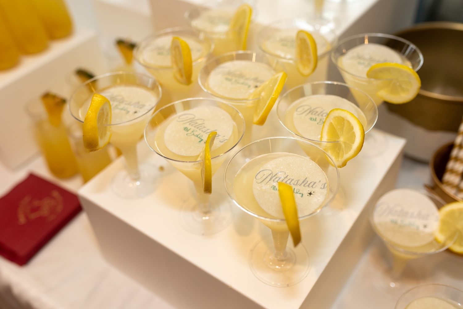 several glasses filled with a yellow beverage, garnished with lemon slices and served on a white tray.
