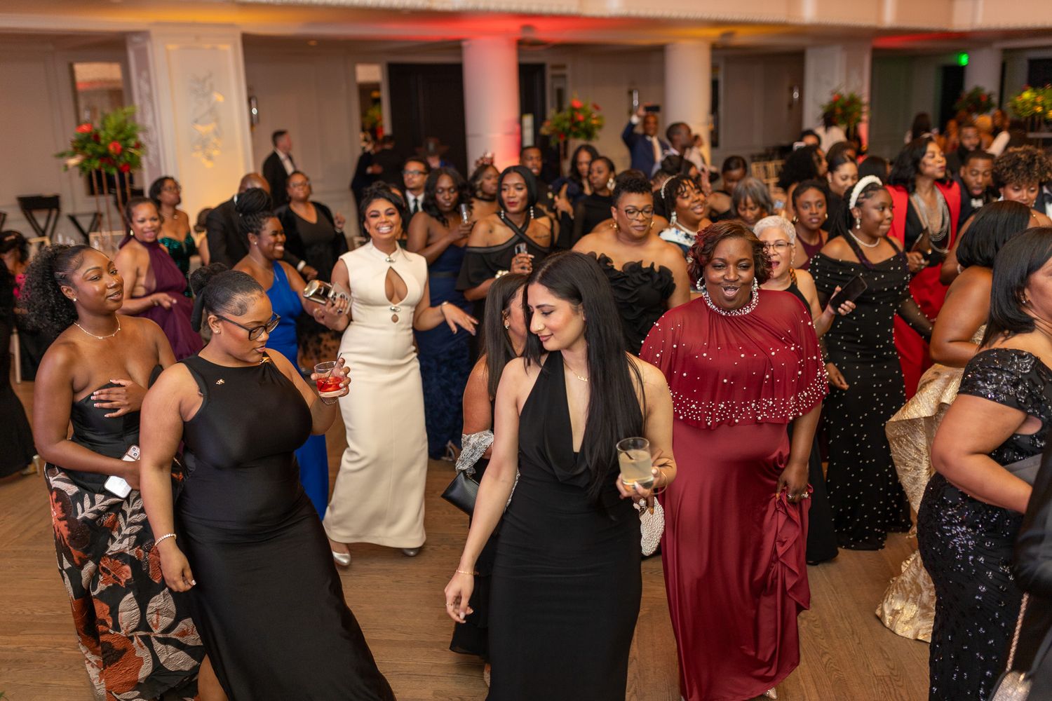 A lively indoor social event or reception with a large group of people mingling and conversing. Guests are dressed in formal attire.